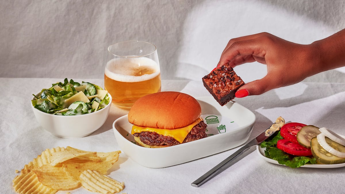a meal of a burger, brownie, salad, and chips on a white tablecloth