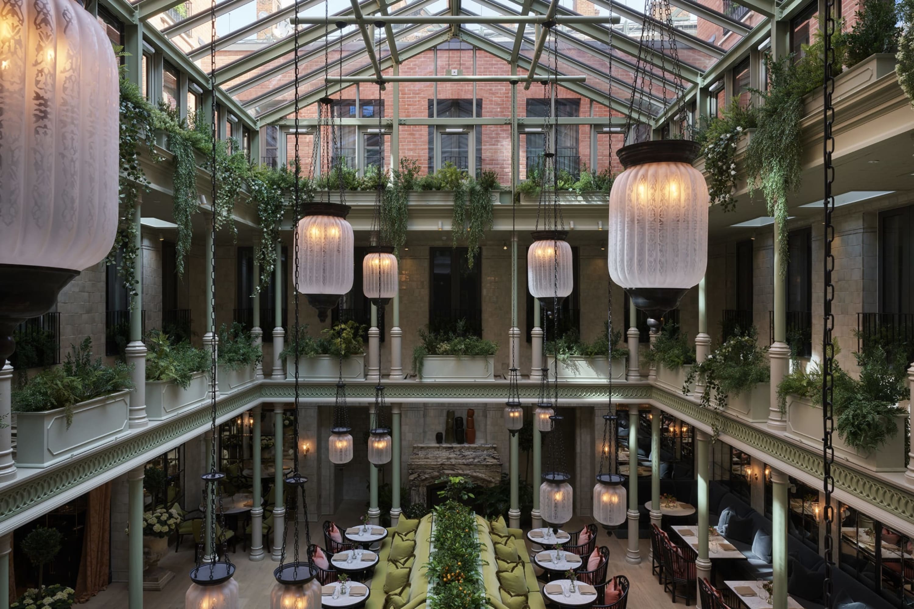 A glass-pyramid-roofed atrium with vine-lined railings, elegant light fixtures and high-end restaurant table settings on the lowest level