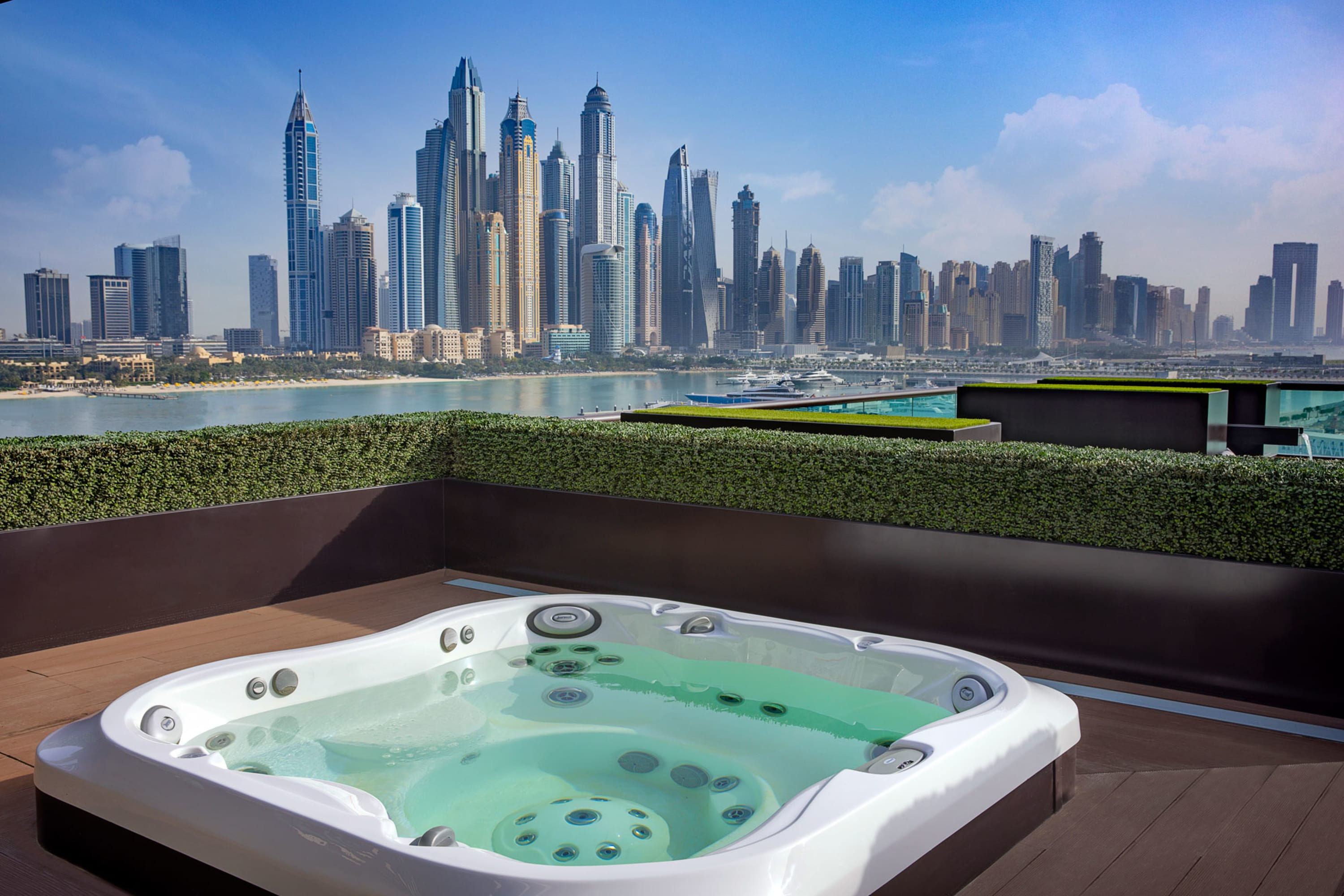 A spacious hot tub on a terrace lined with hedges. The Dubai skyline stands prominently in the background