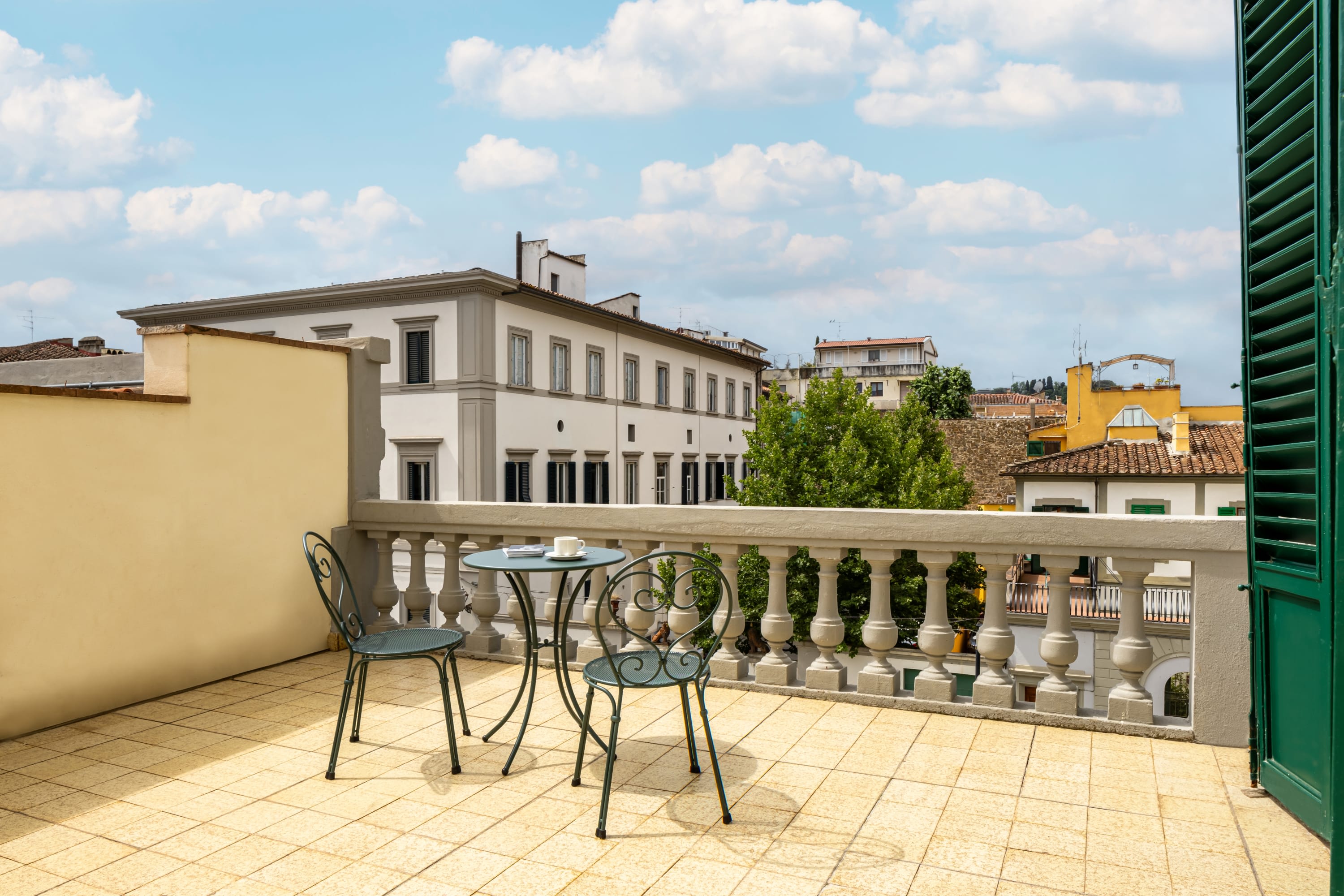 Two iron chairs on a spacious private balcony overlooking some historic buildings in Florence