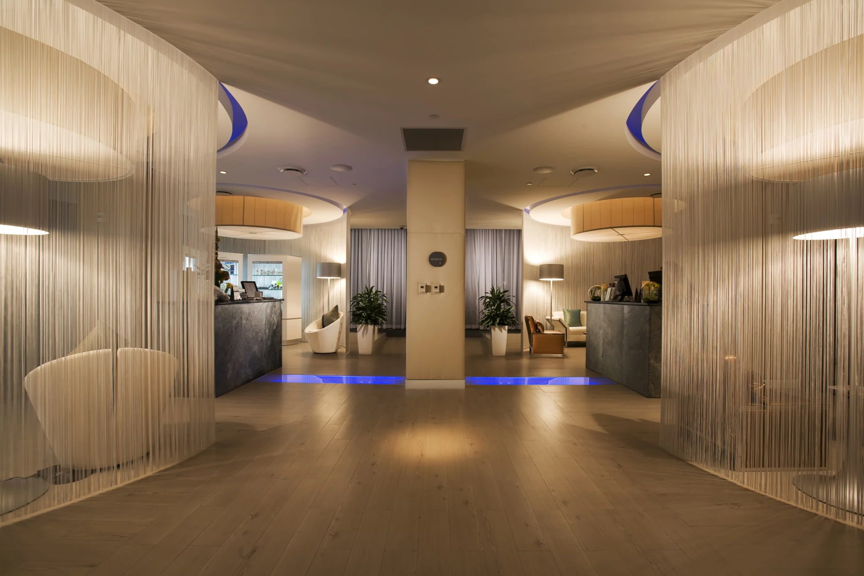 Elegant lobby area with sheer curtains sectioning off waiting area seating, hardwood floors, and chic potted plants