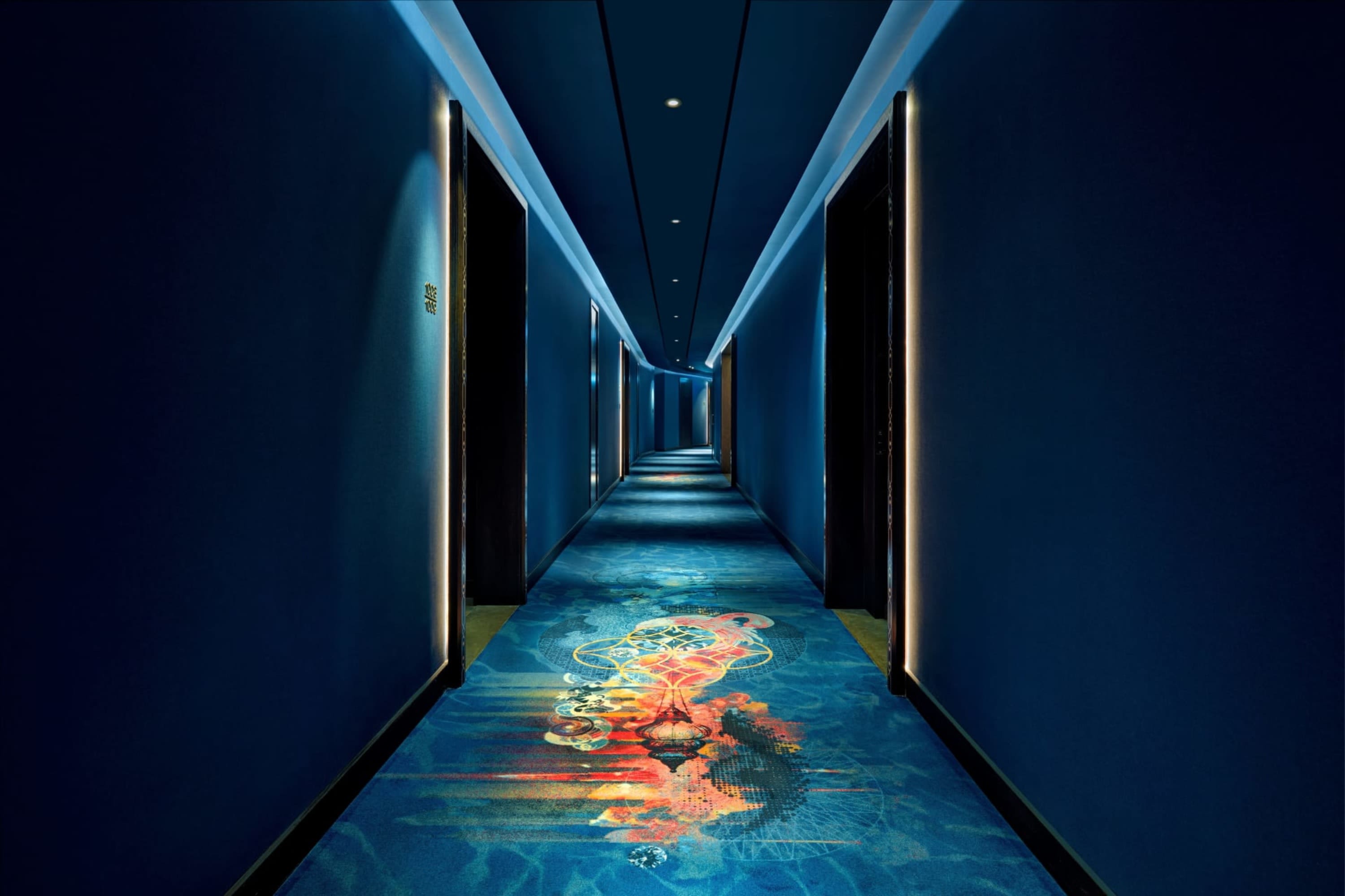 Deep-blue hallway with neon-lit door frames and carpeted floors with an exceptionally intricate design of a Moroccan lamp