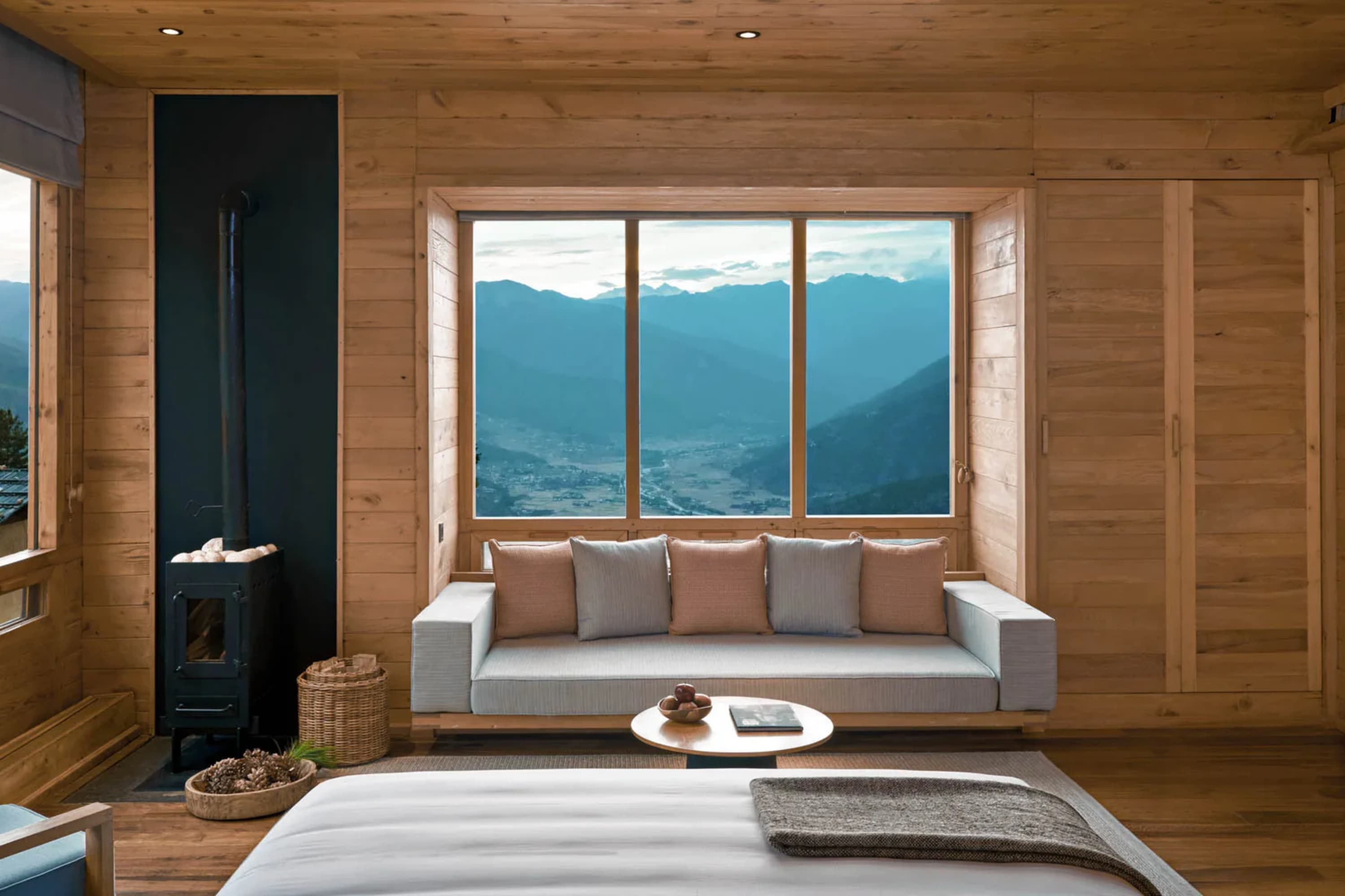 A mix of rustic design and chic luxurious furnishings in a hardwood walled and floored lodge living area with incredible views of a valley and ravine