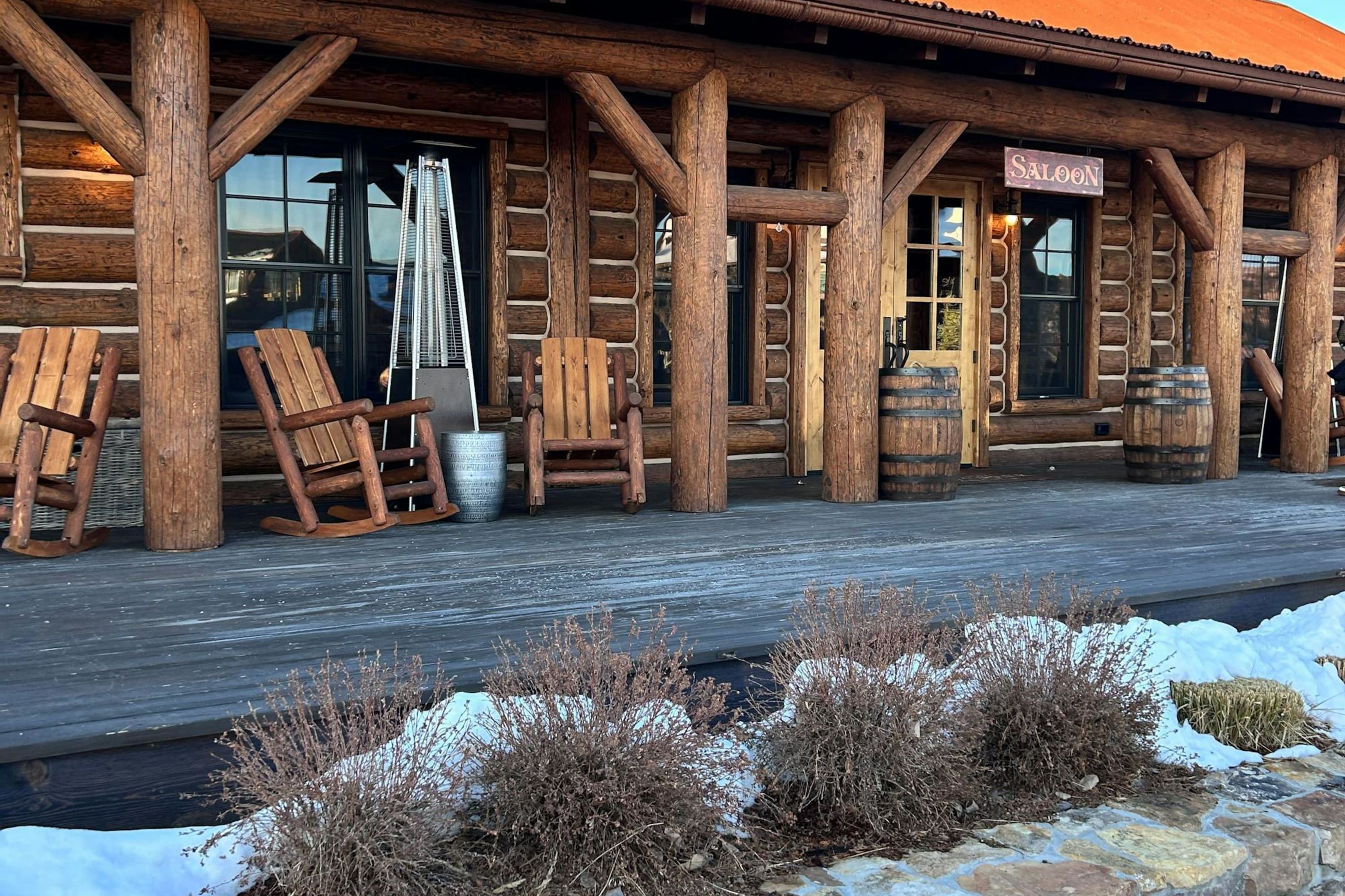An Old Western building with wooden furniture, barrels and a sign reading "saloon." Snow dusts the ground.