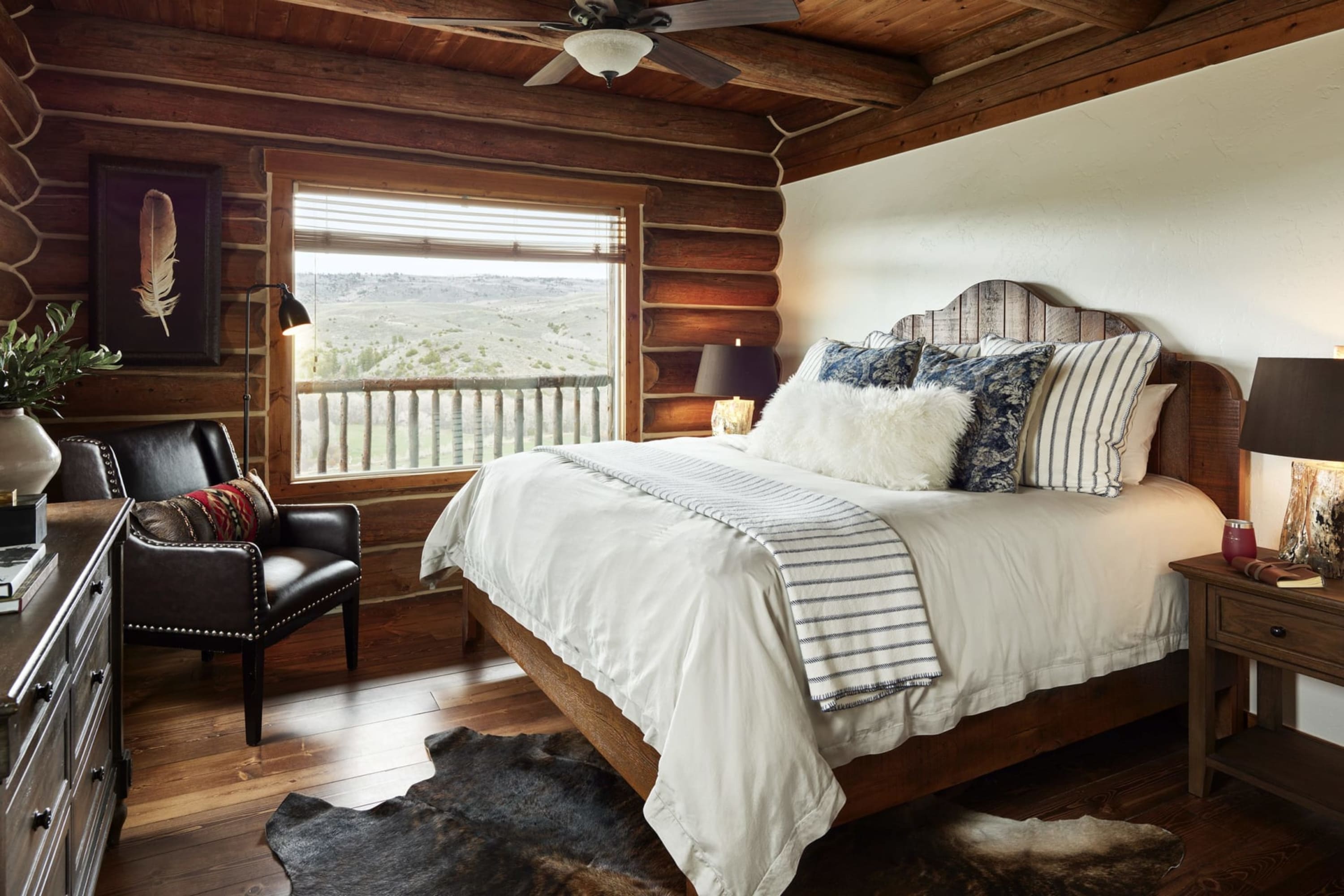Rustic decor fills a log-wall cabin room while a view reveals a wide-open, green plain with mountains in the distance