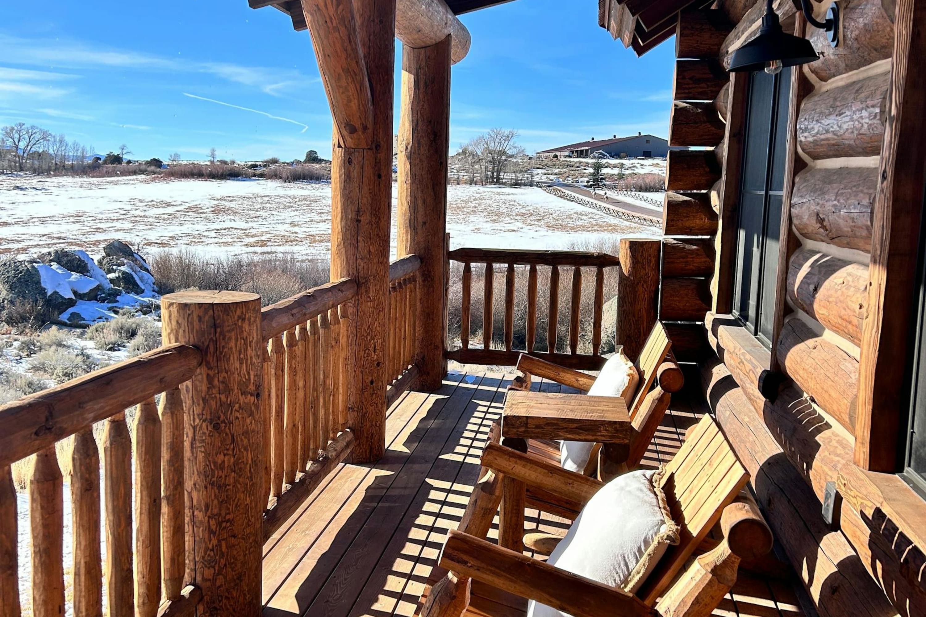 Twin chairs sit on a wooden- and log-made patio with a dusting of snow on the surrounding grounds