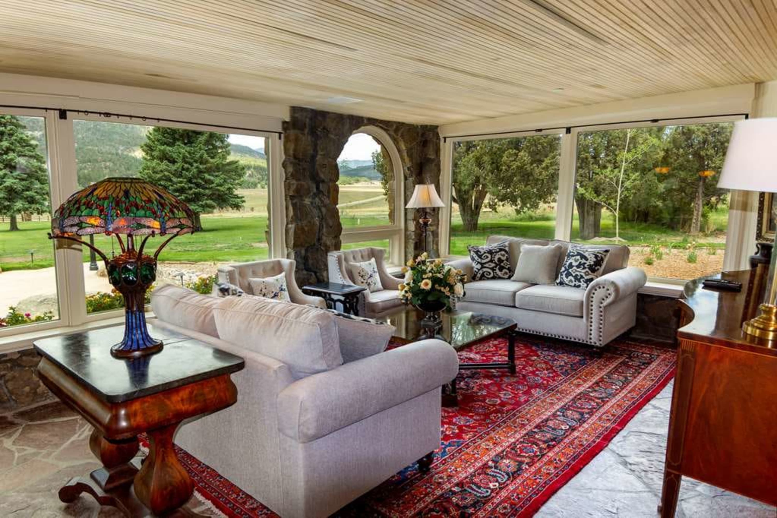 Elegant classic decor fills a lounge area with massive bay windows revealing the verdant resort grounds of Vermejo