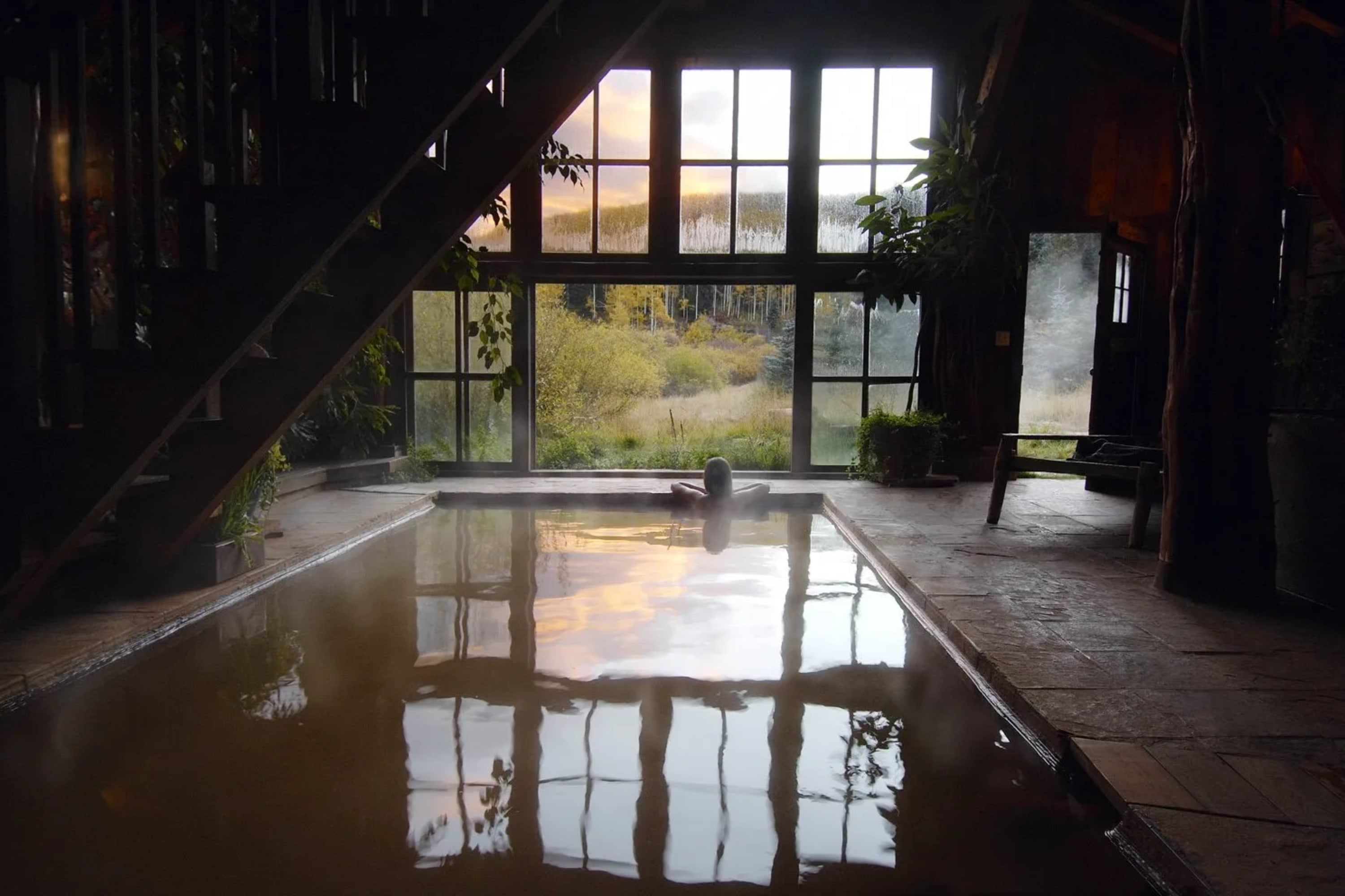 A lone woman sits in a hot spring with a pool-like enclosure, staring out into the Colorado wilderness