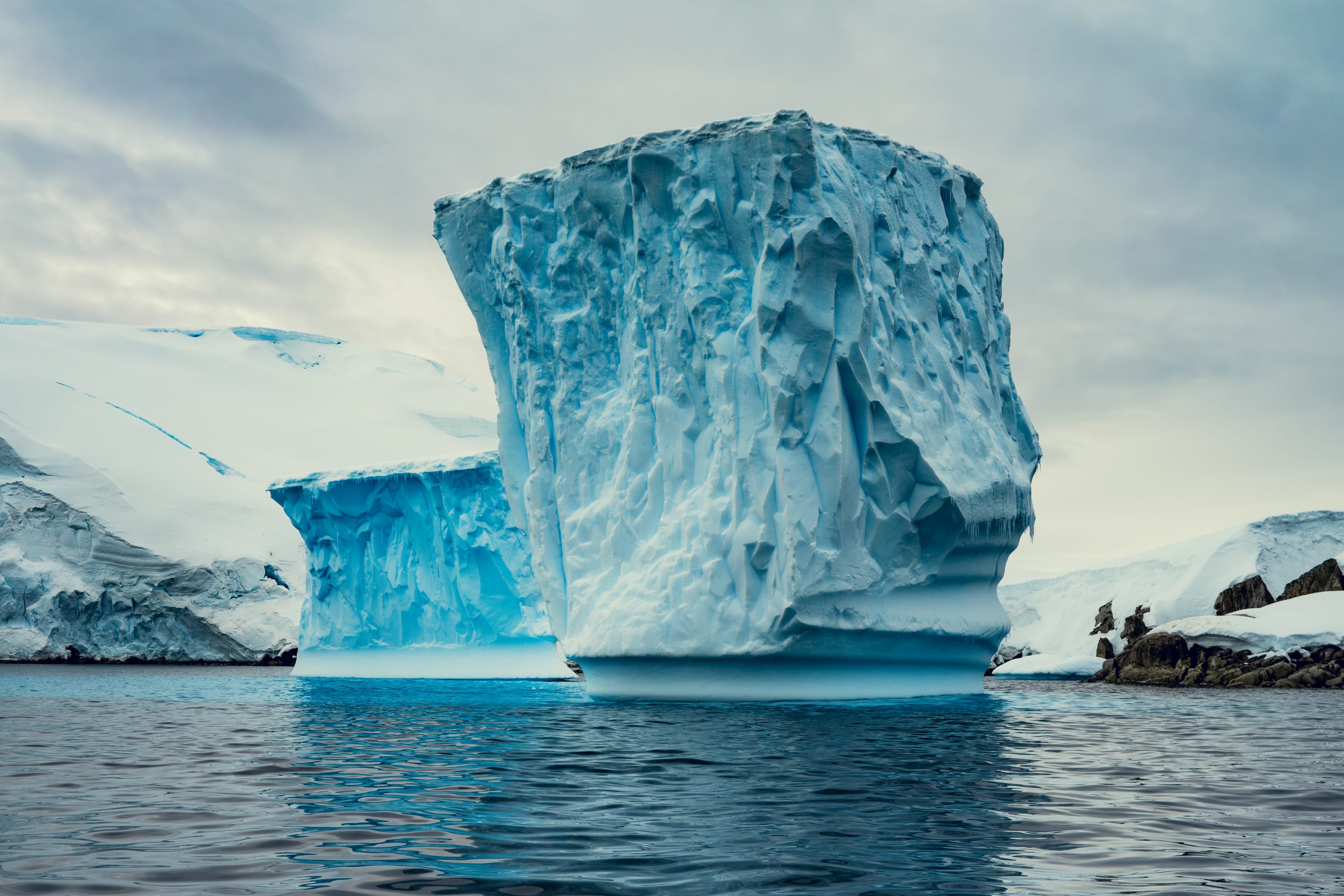 Brilliant blues contrast with deep blues and whites in a few icebergs floating on calm water