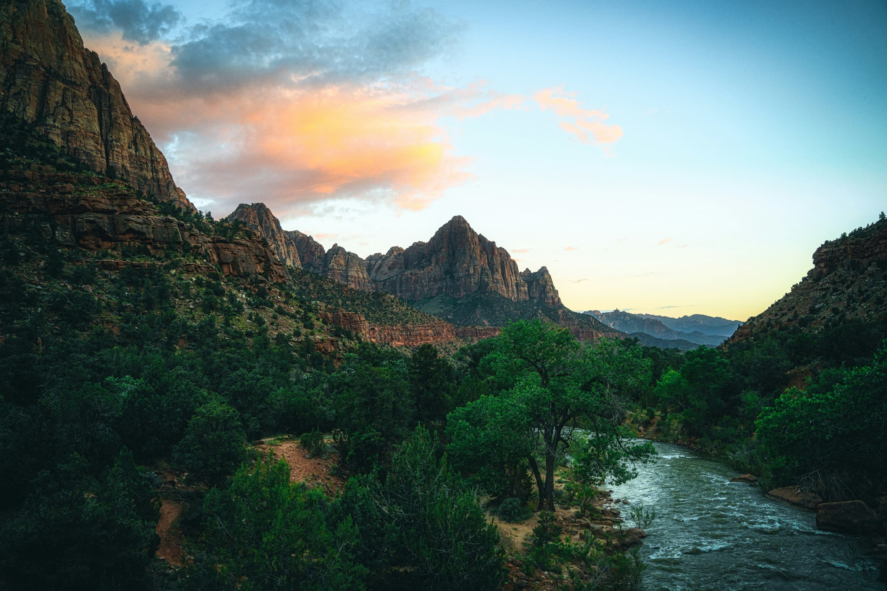 At twilight: trees and a rushing stream buffeted by rocky mountains