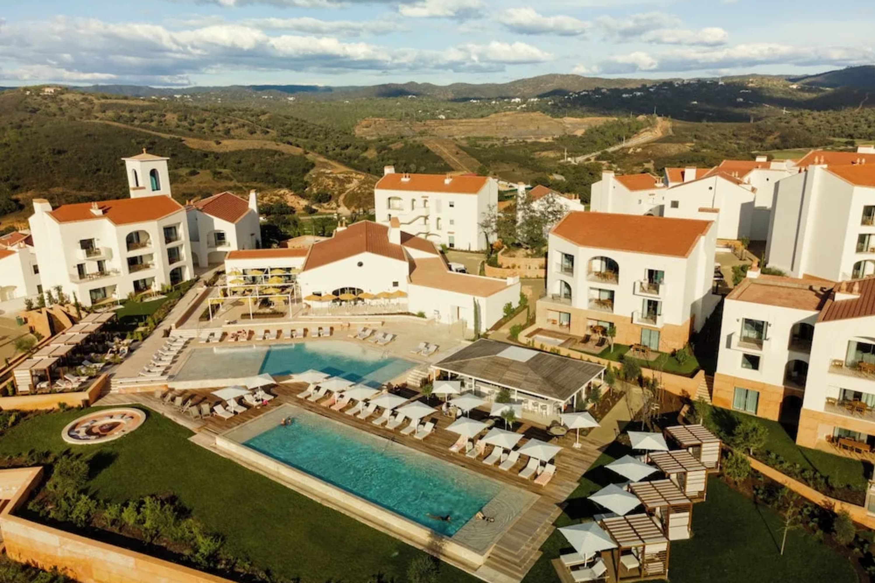 Orange tile-roofed, whitewashed luxe resort buildings with massive pools set on rolling hills