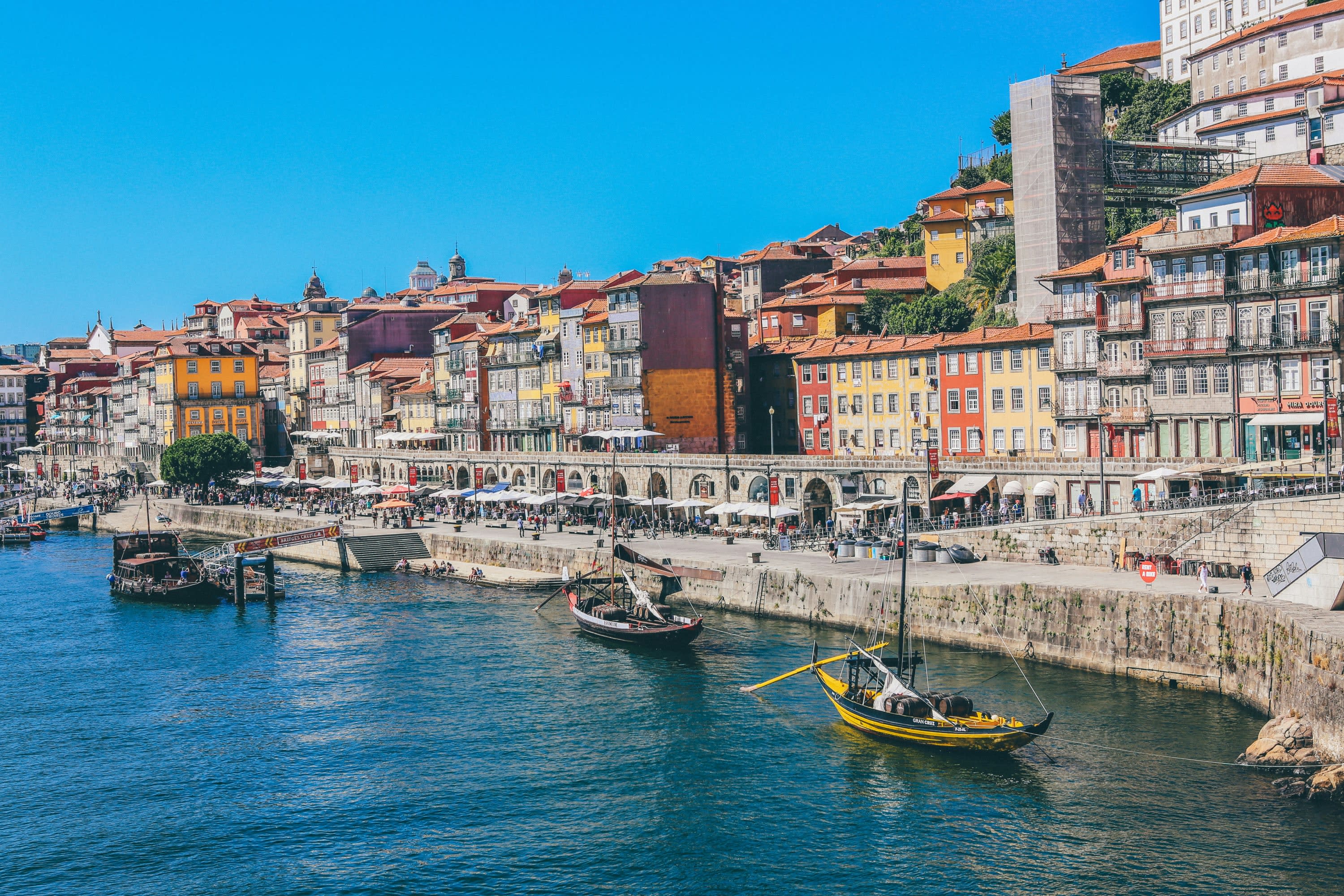 A variety of colorful, historical sailboats moored next to the waterfront of Porto, with its colorful buildings and lots of street vendors