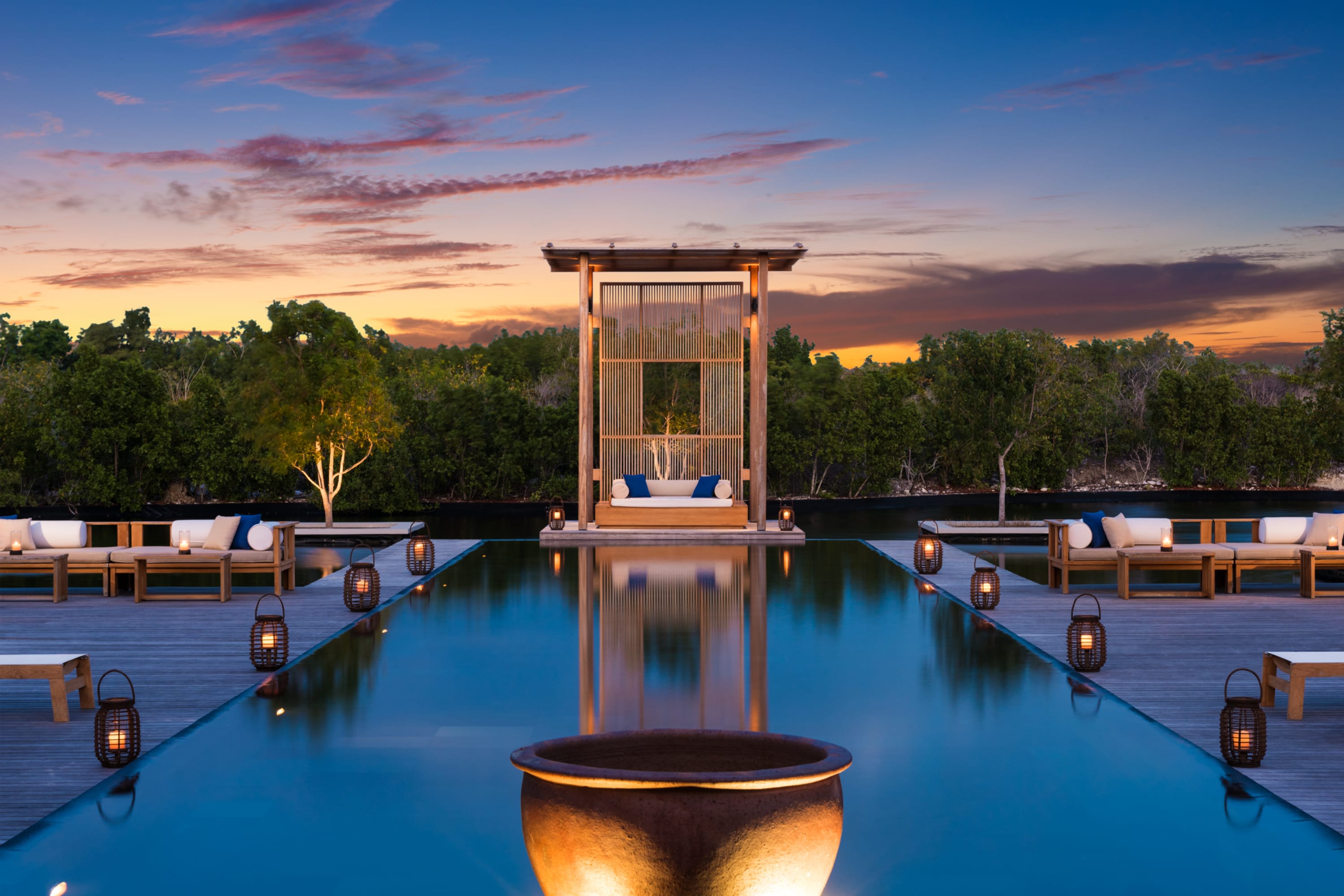 Design-forward pool area lined with unusual lanterns, chic loungers and soft-hue hardwood, all surrounded by trees