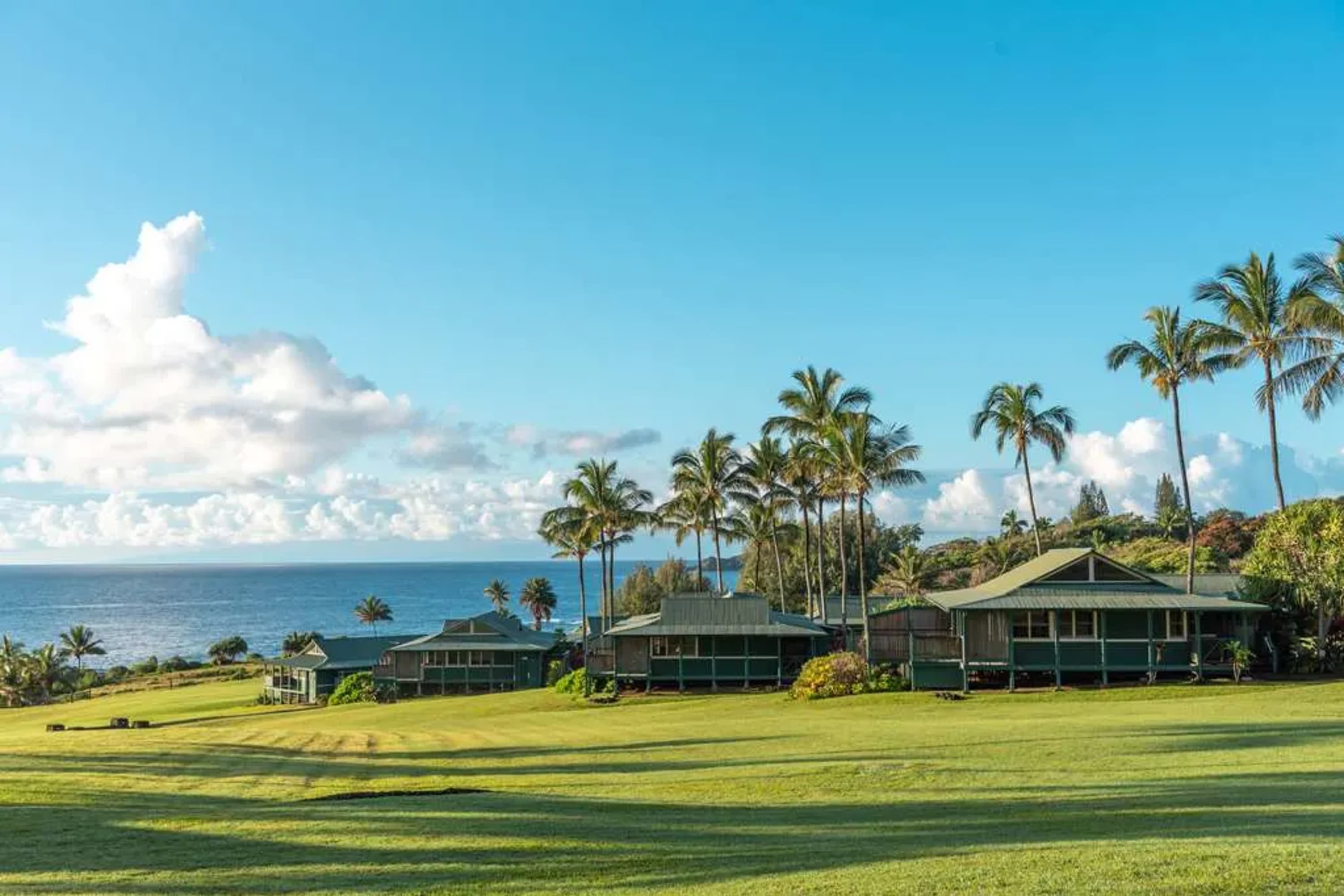 Manicured grass leads up to island-themed cabins overlooking the Maui coastline