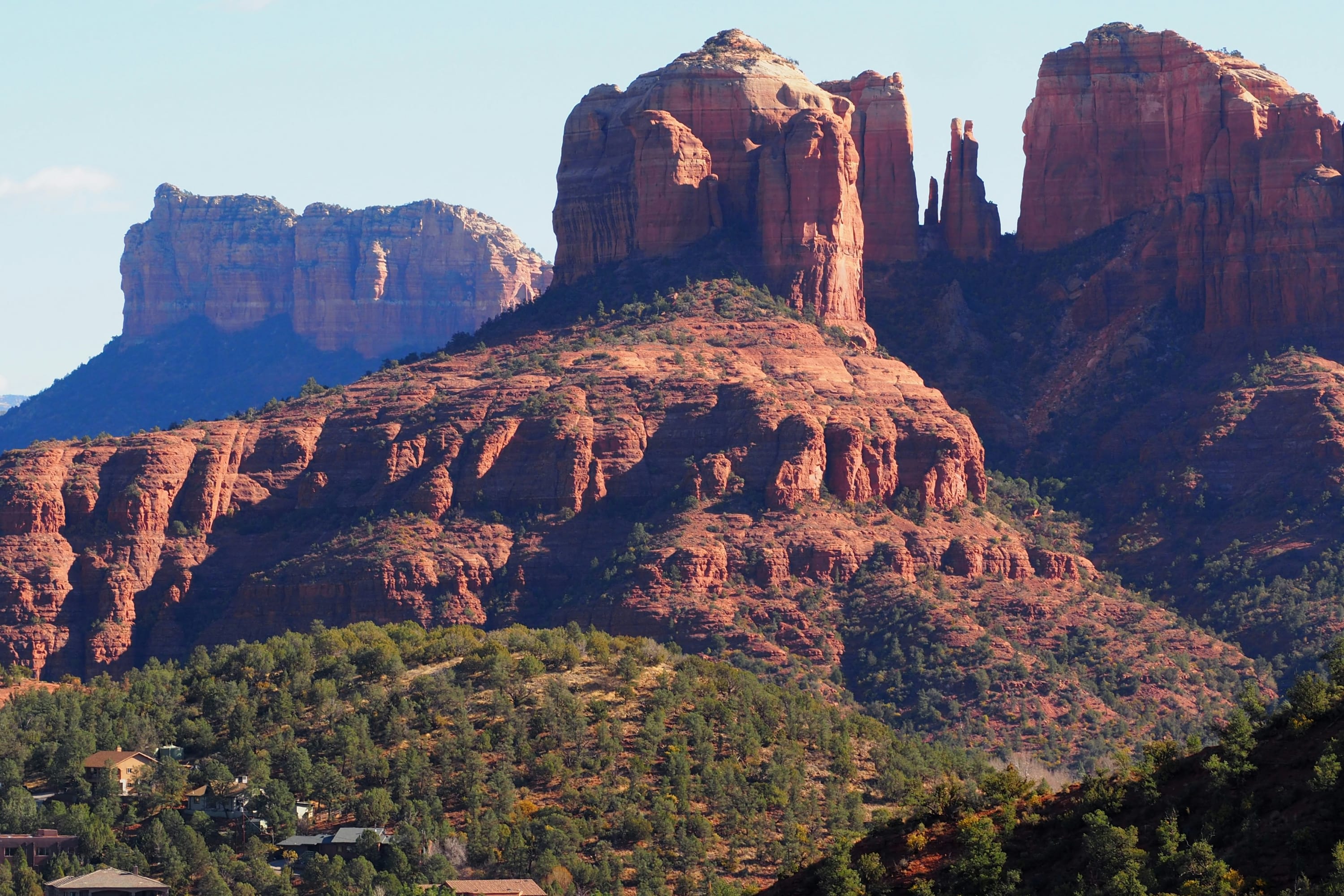 Dramatic red-rock mountains rise up over a sparse green forest