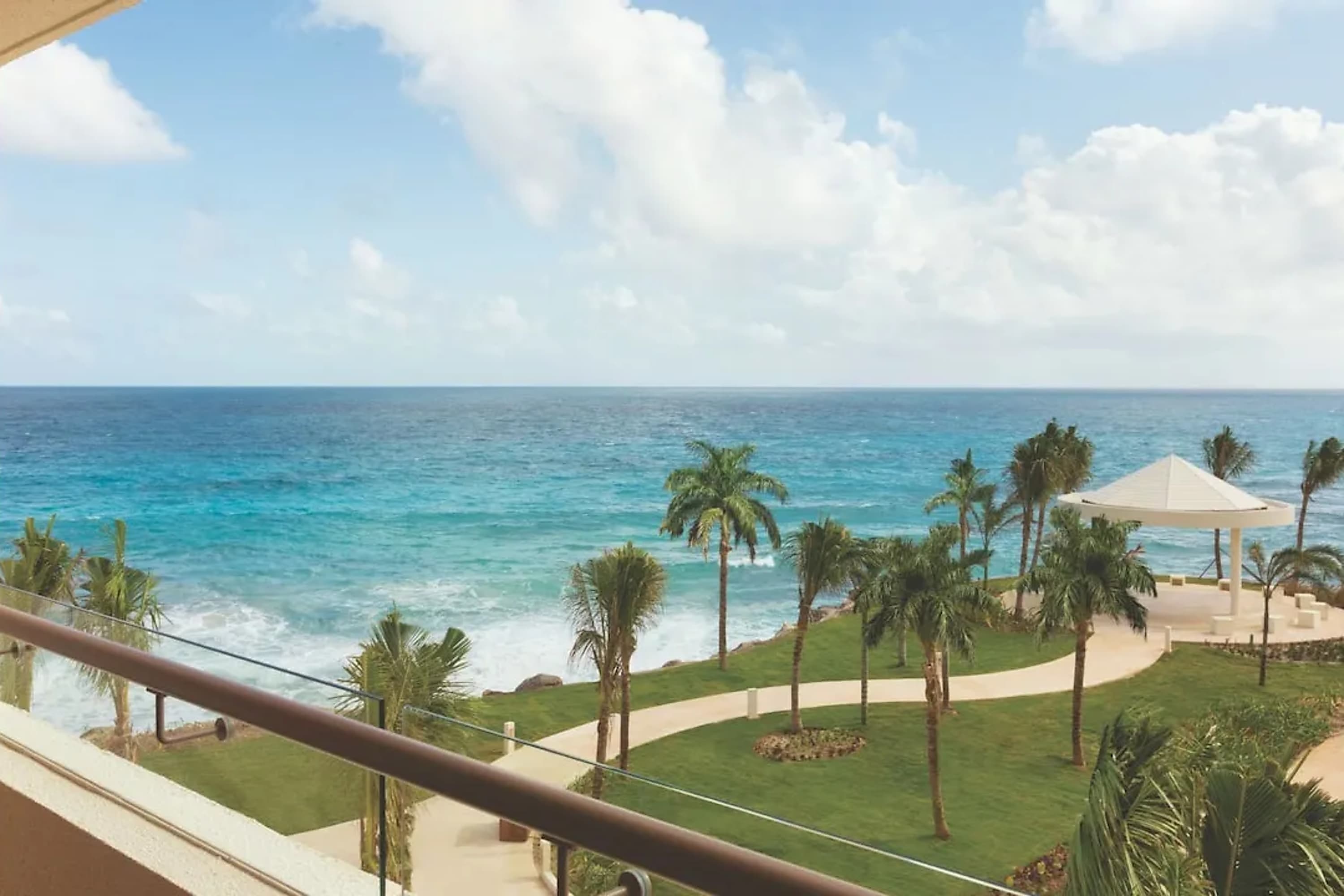 Waves crash down on a rocky beach before well-manicured resort grounds with palm trees