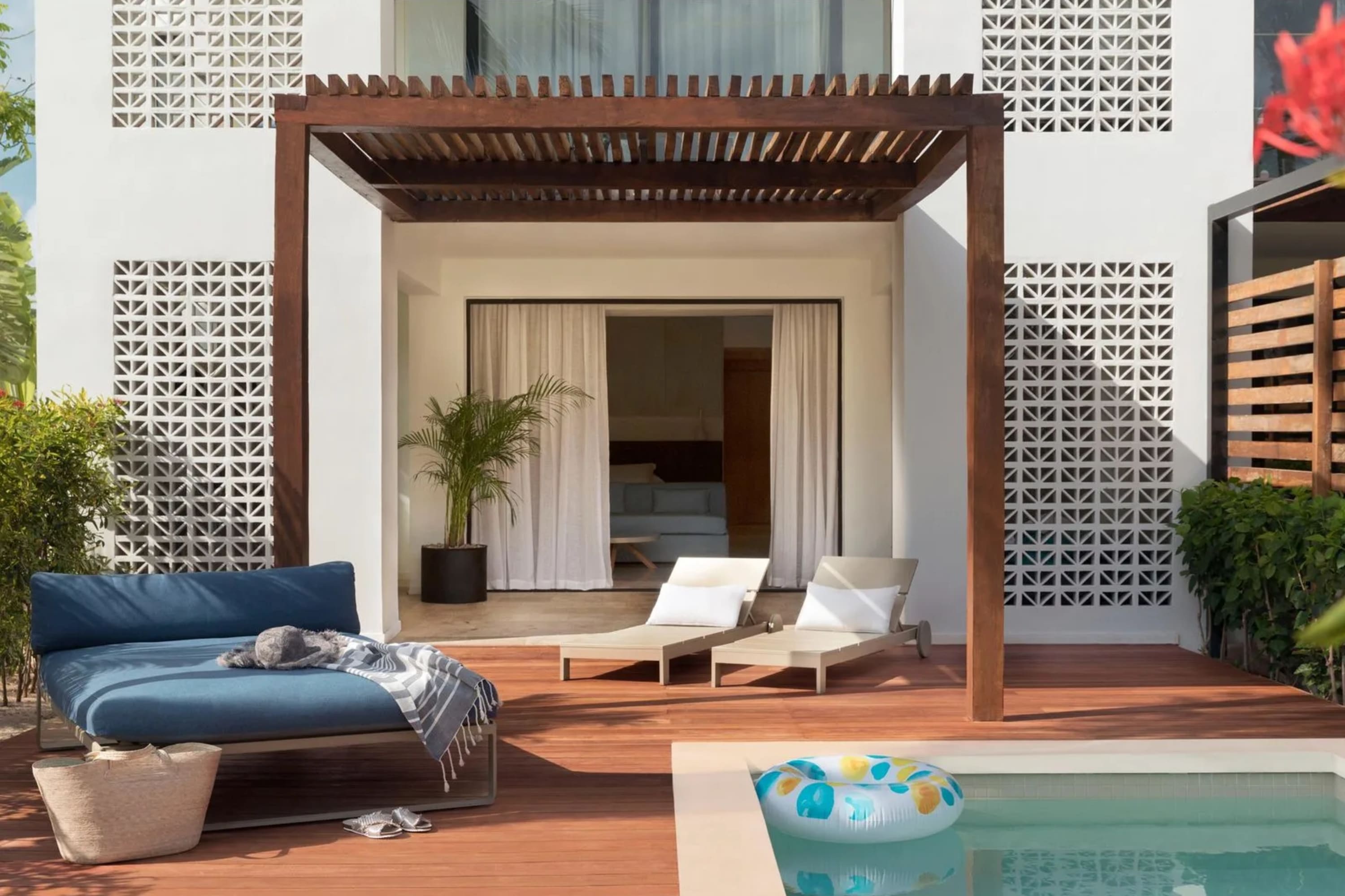 A day bed and lounge chairs on a patio with a pool float floating in a pool
