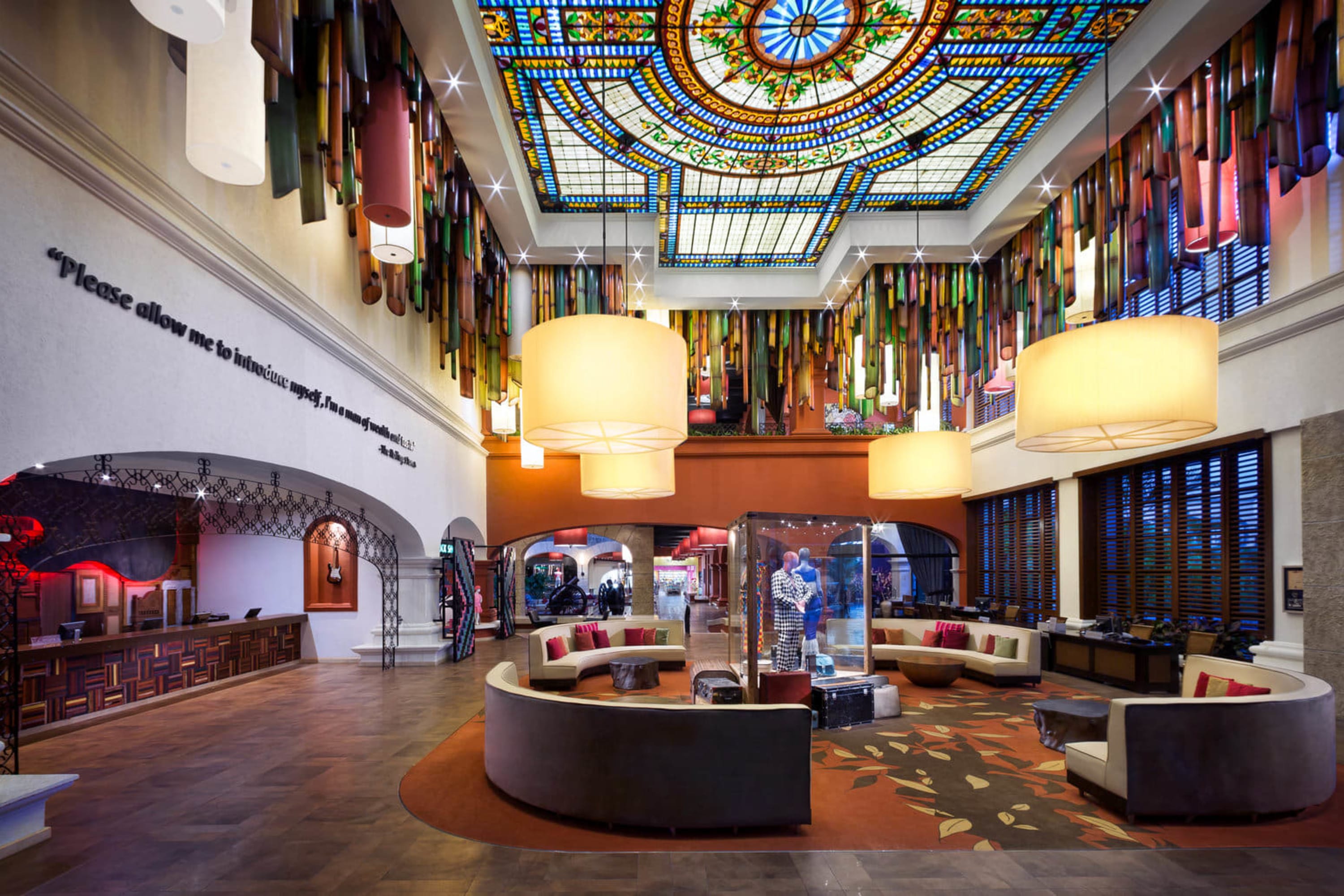 Wind-chime like light fixtures hang from a ceiling with a stained-glass window at the center. A couple of artists worn by music artists are on display. And contemporary furniture fills a spacious and comfortable lobby