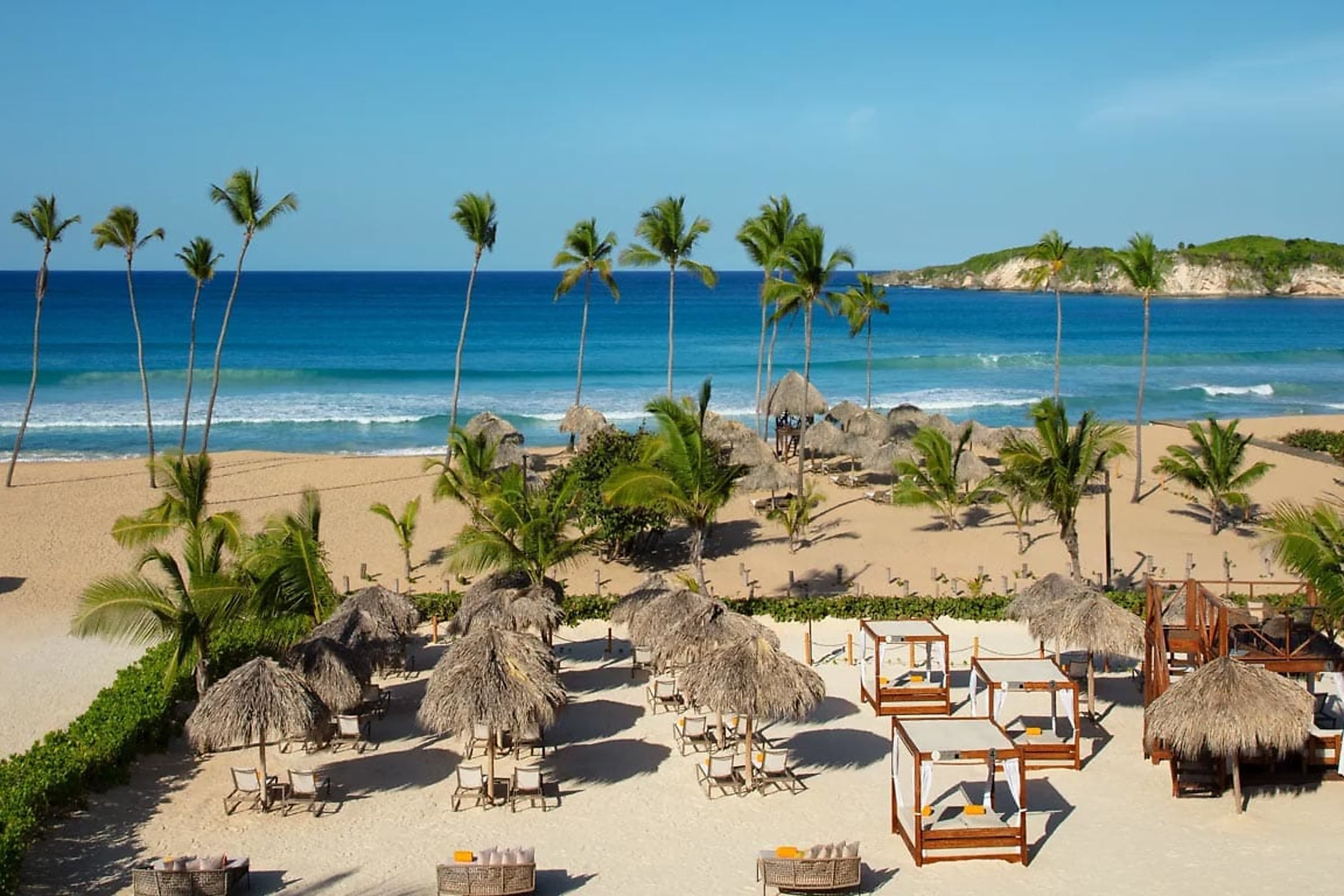 Thatch umbrellas and cover beach chairs on a white-sand beach before a calm ocean