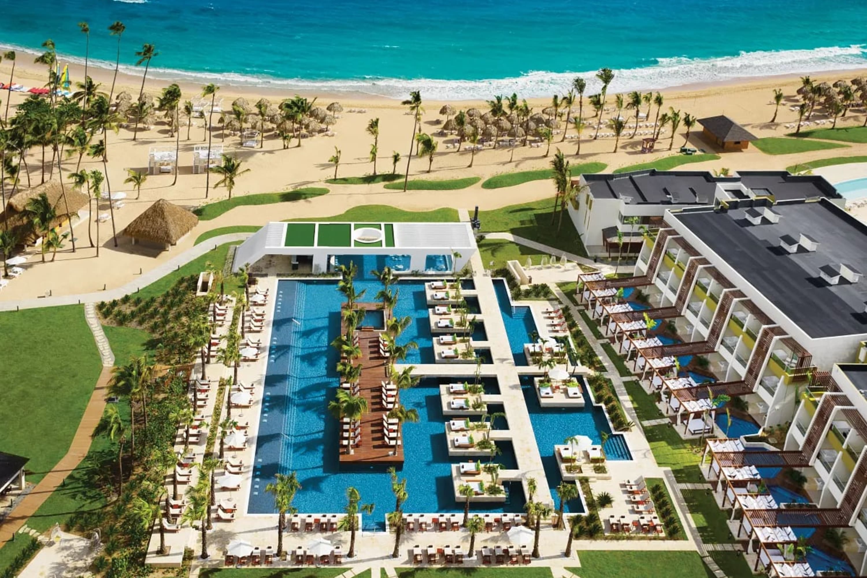 A large pool complex next to a white-sand beach with palm trees and suites with private plunge pools or hot tubs
