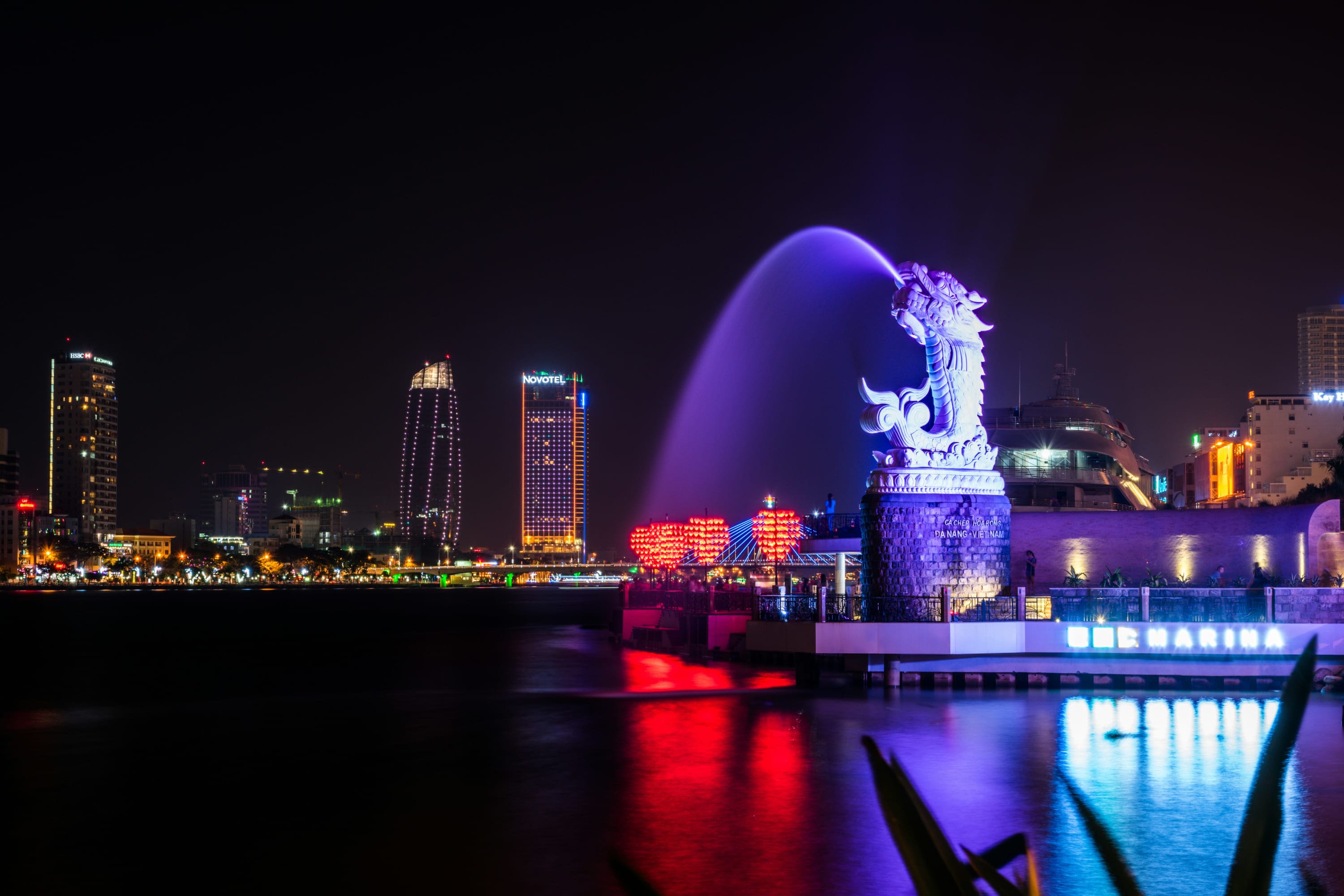 At night: neon-lit dragon spouts water on Da Nang's waterfront with skyscrapers in the background