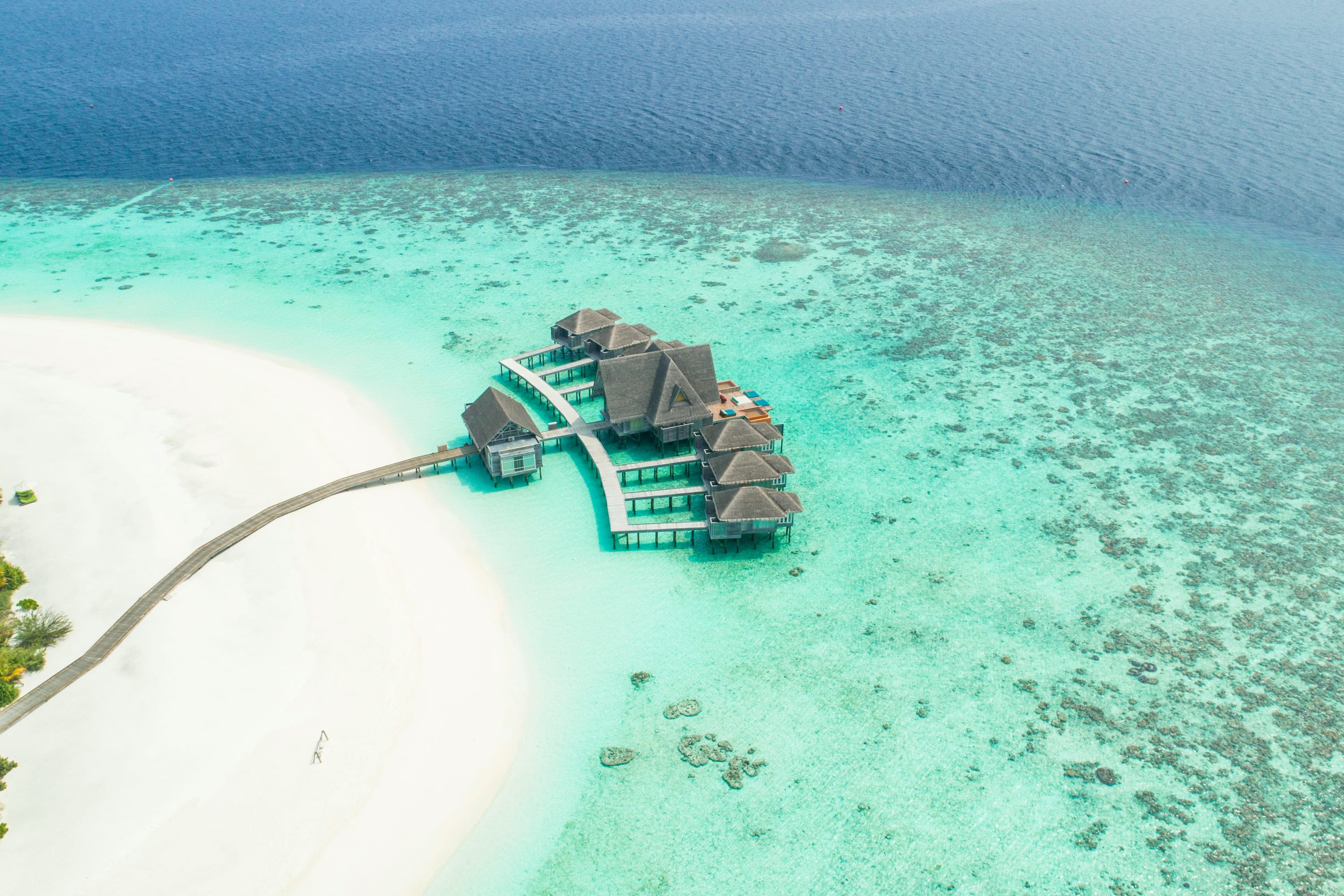 A small group of overwater bungalows in shallow water near a pristine white-sand beach