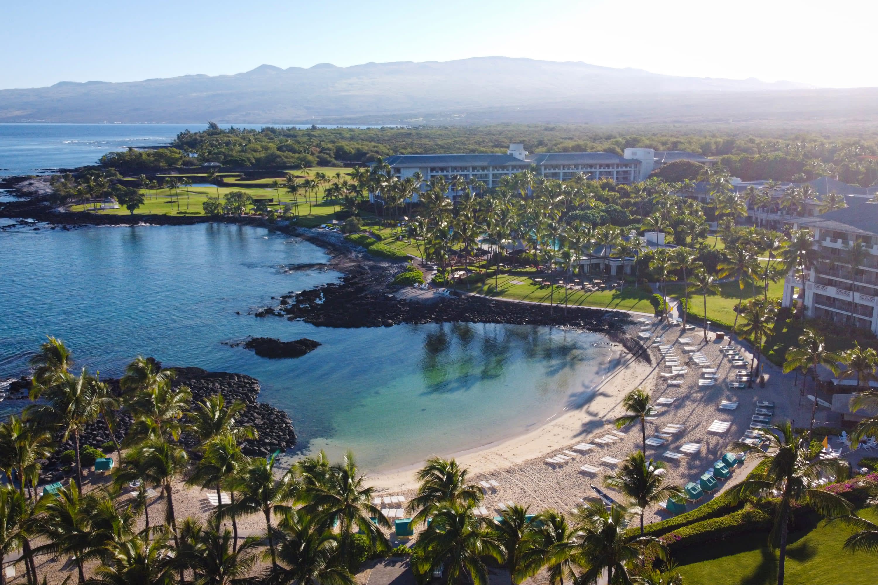 Aerial view of expansive tropical resort grounds, a private lagoon and clouds partially concealing mountains in the distance