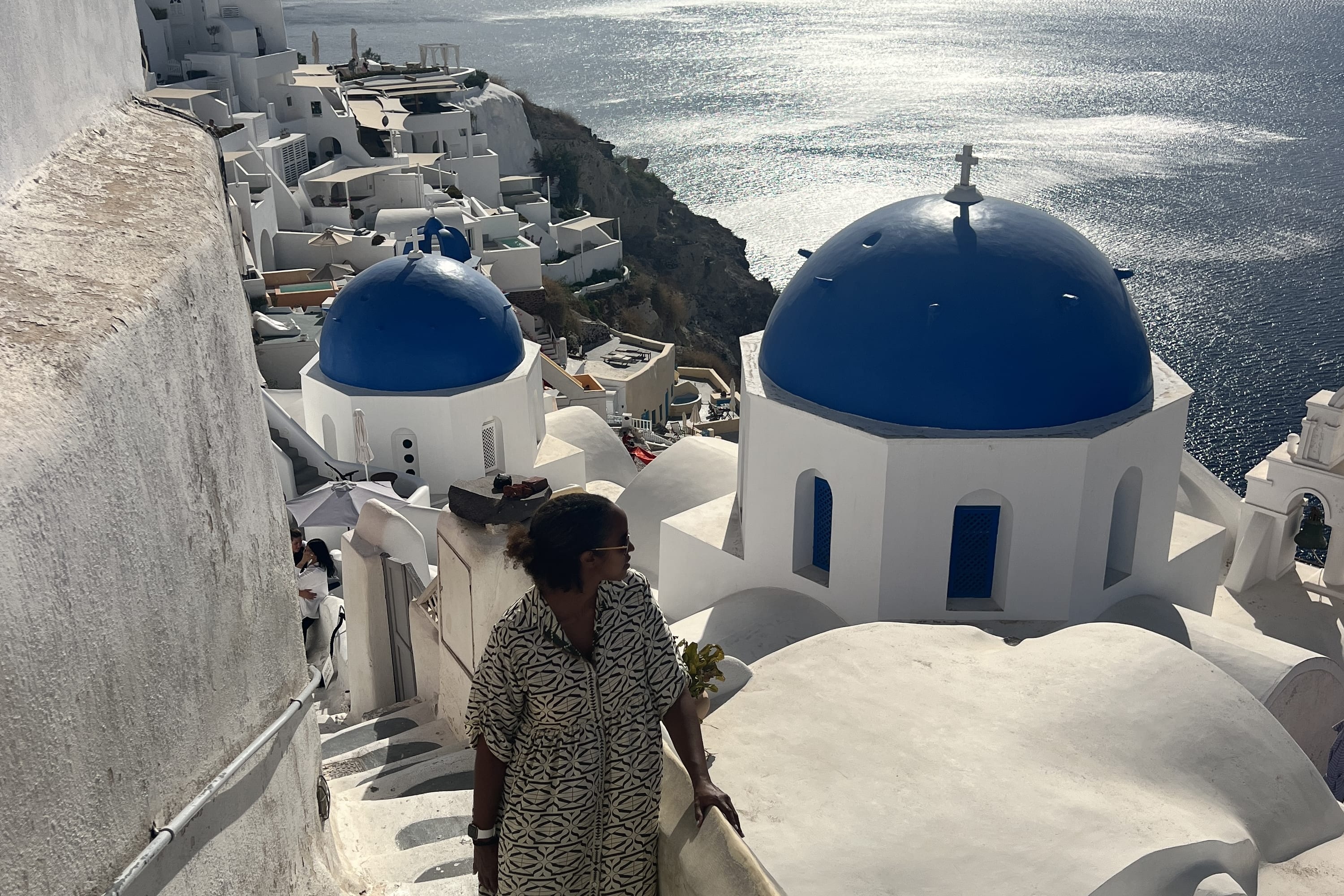 woman standing on a white staircase overlooking the sea and blue-domed buildings