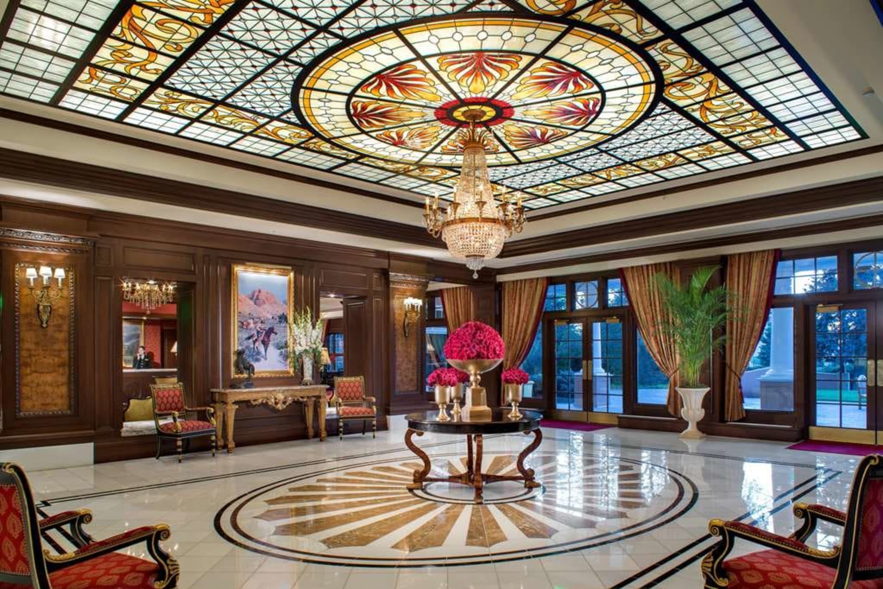 Grandiose lobby area with a crystal chandelier, elegant vintage furniture, marble floors, an ornate stained-glass ceiling and hardwood walls