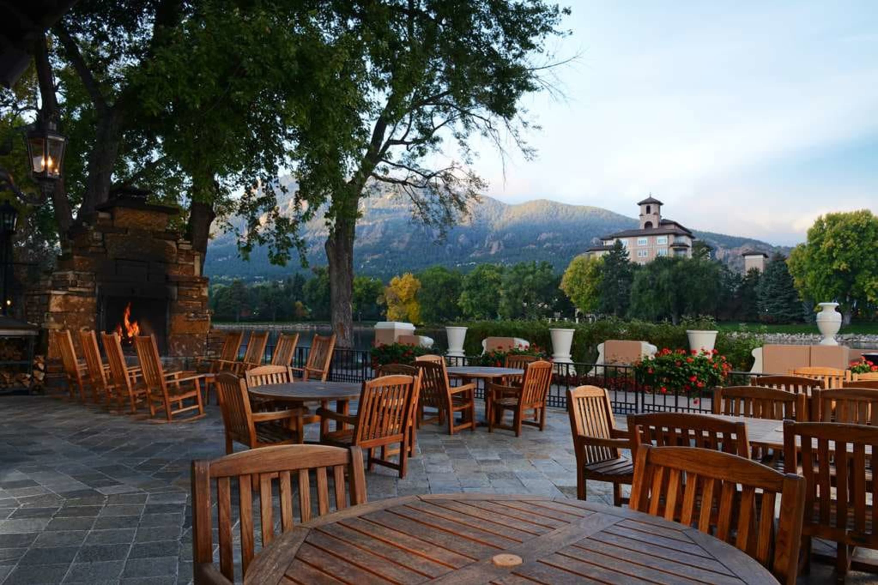 Rustic chic tables and chairs on a stone patio warmed by a fireplace and surrounded by lush greenery
