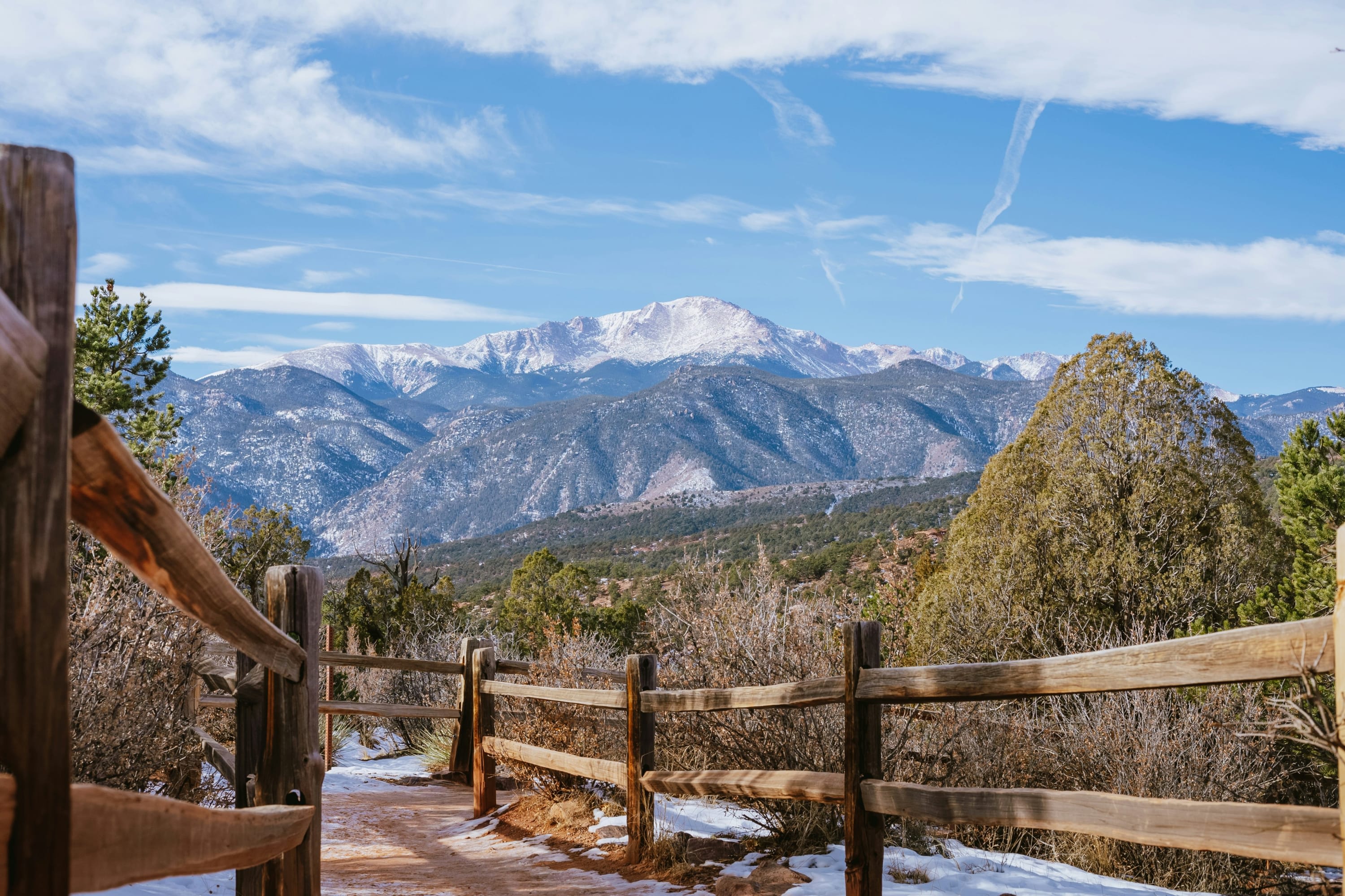 Wooden fences line a dirt path through brush with mountains in the far distance capped by snow