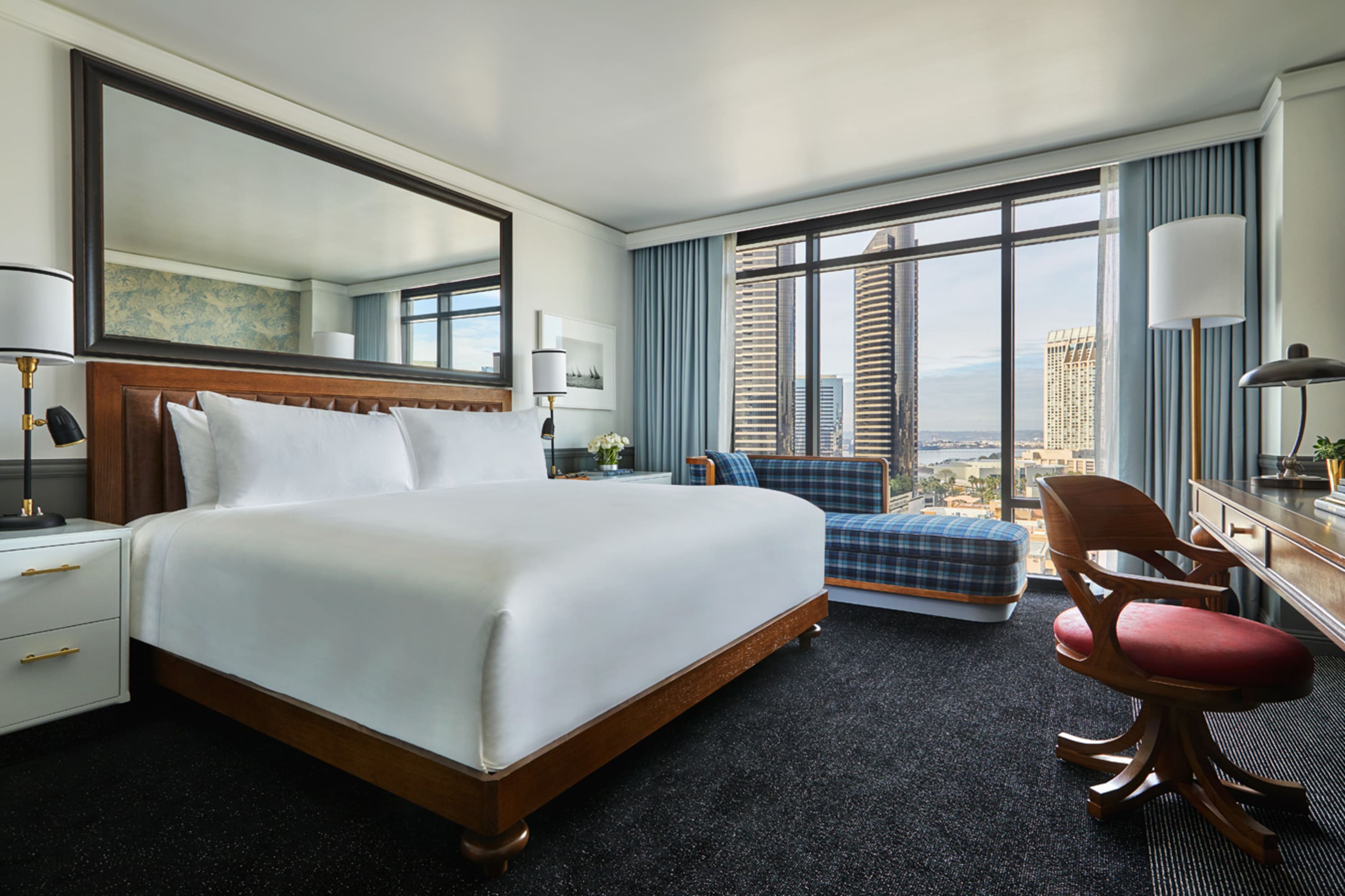 Stylish room with whitewashed bedding, a vintage-style office chair, a plaid chaise lounge and a large