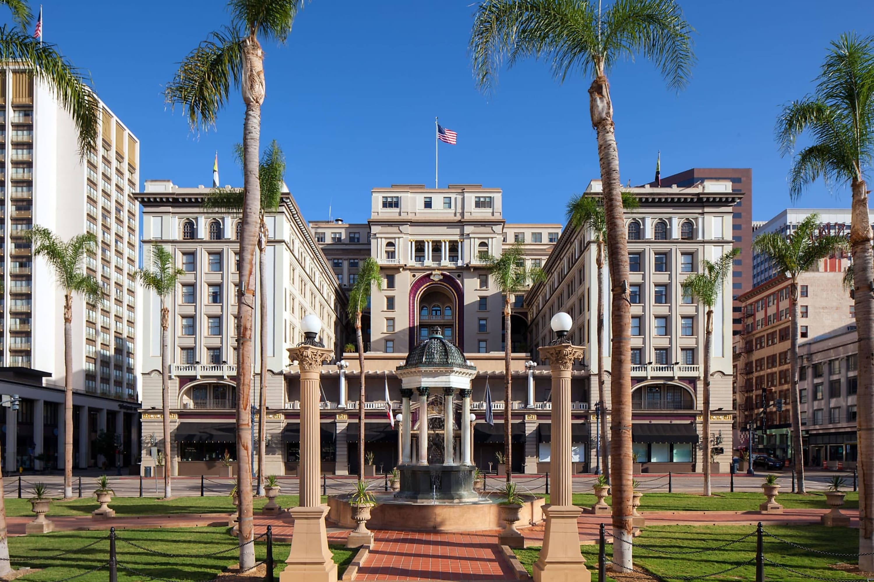 Palm trees intermixed with neoclassical columns surrounding a water fountain in front of the Us Grant in downtown San Diego