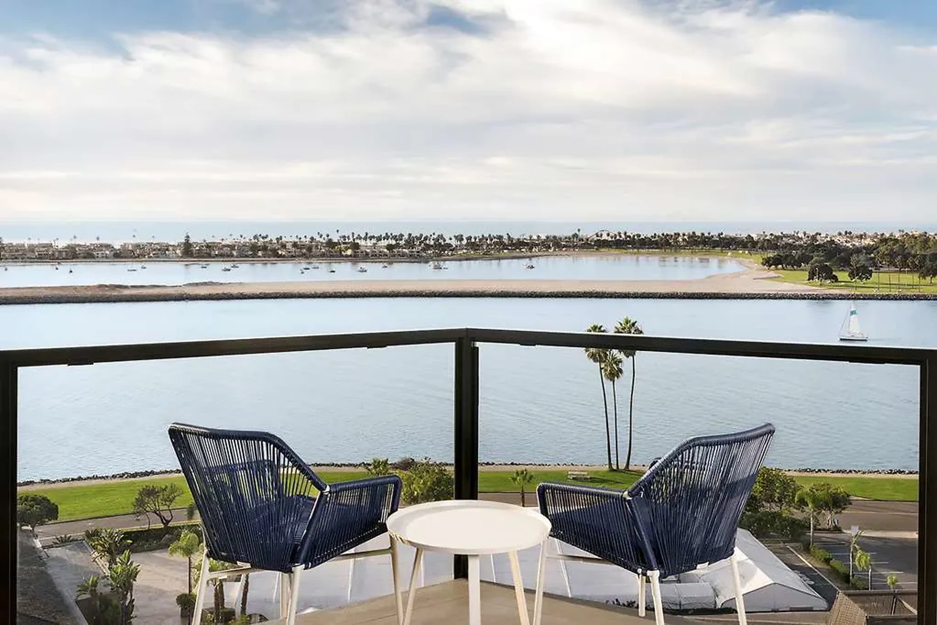 Twin chairs on a balcony overlooking a calm lagoon with a sandy beach on the opposing side