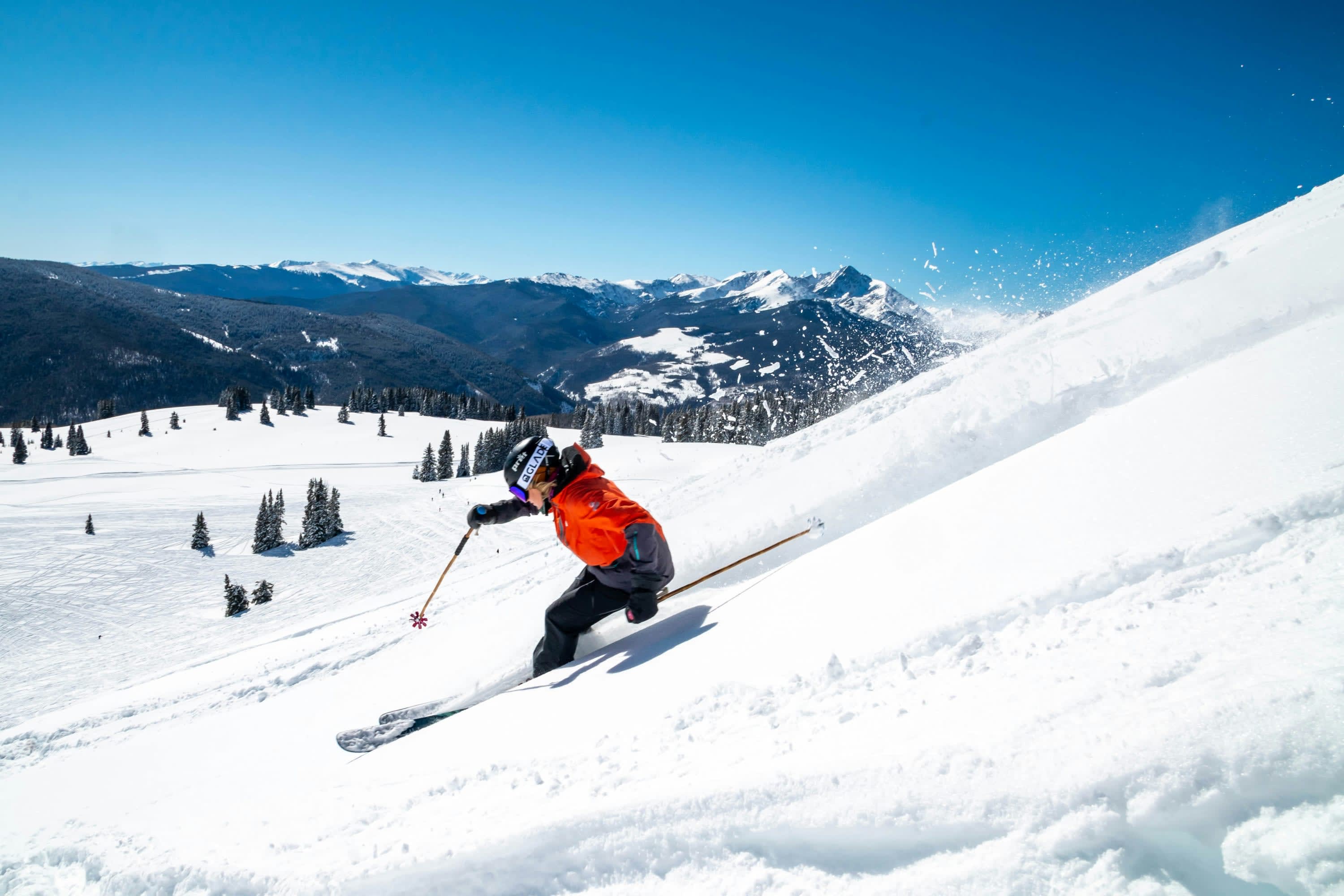 A skier in an orange jacket descends white slopes