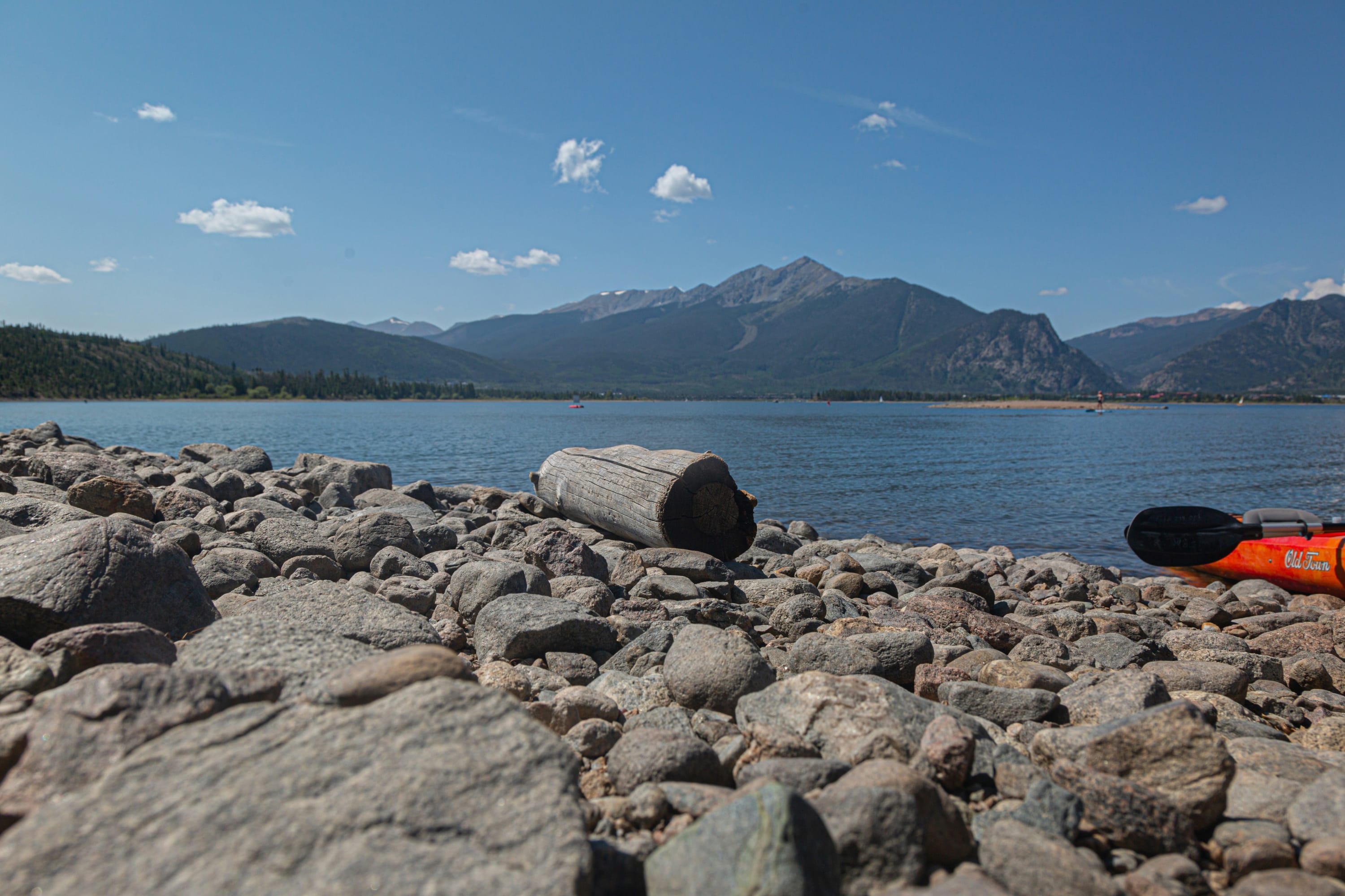 A piece of driftwood occupies the focal point, with a large lake behind and a kayak off to the side