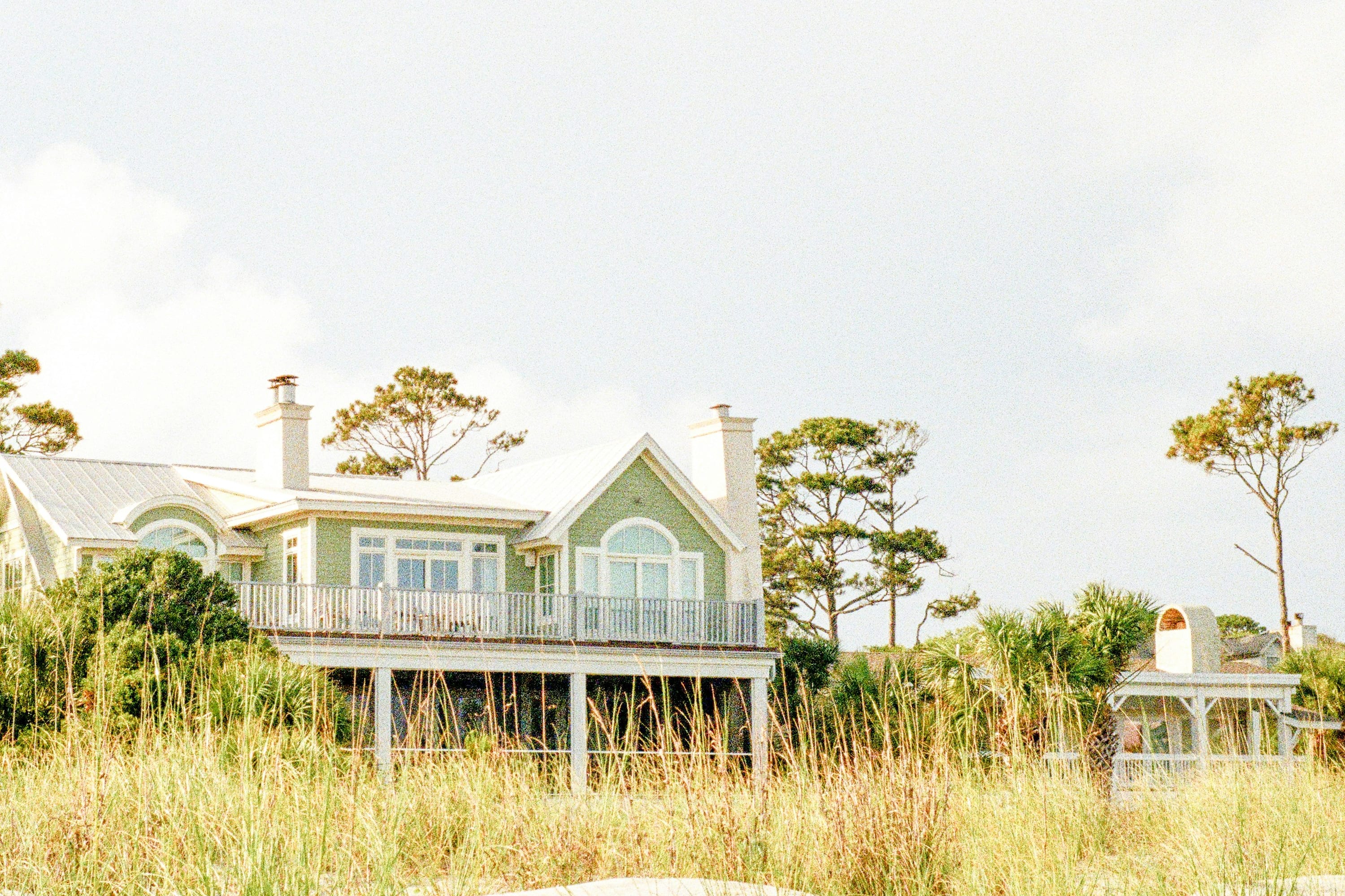 A large beach house with whitewashed accents surrounded by seagrass on a quiet and cloudy but scenic day