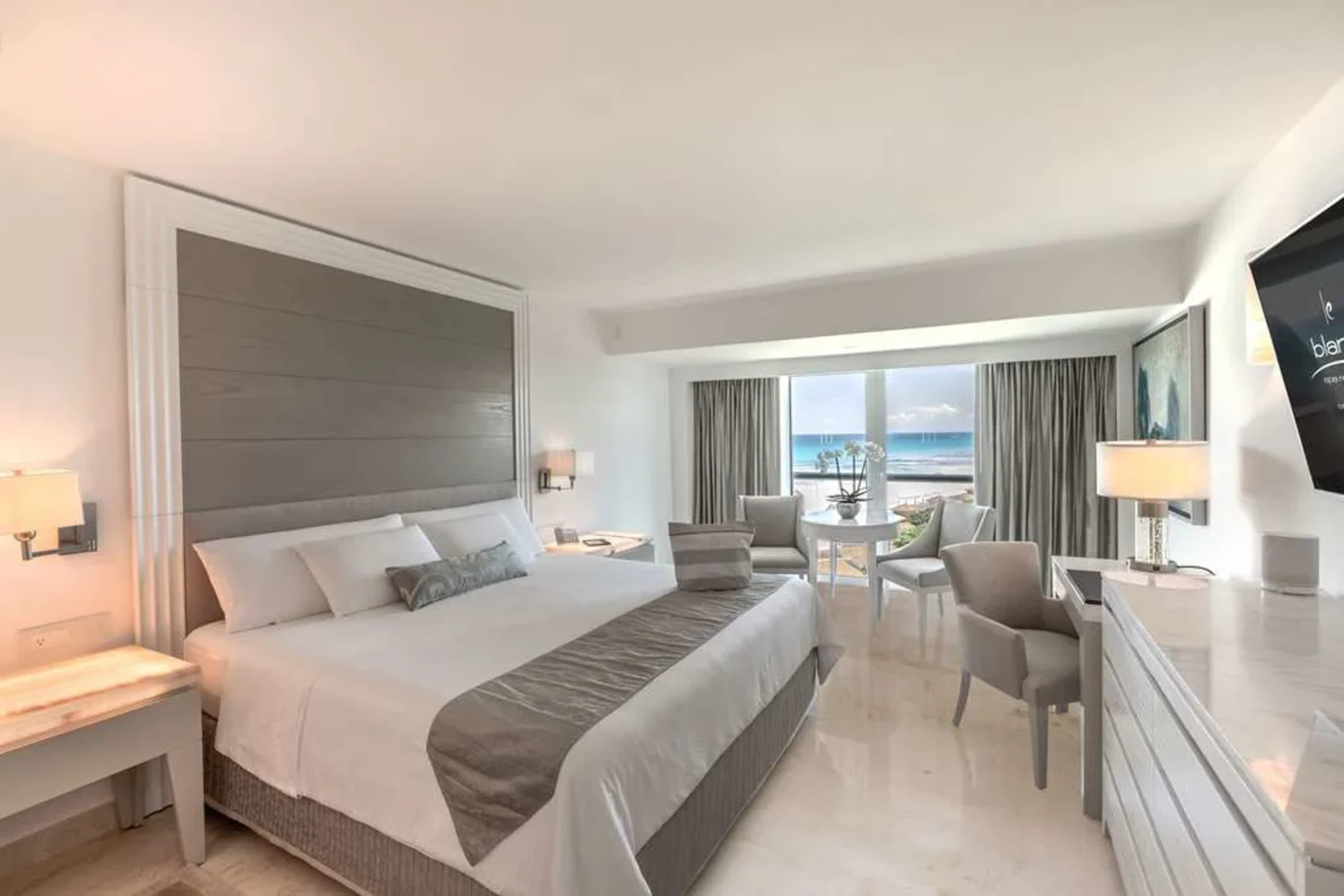 Simple room with nice furnishings and a neutral color palette. Large windows reveal the ocean and beach