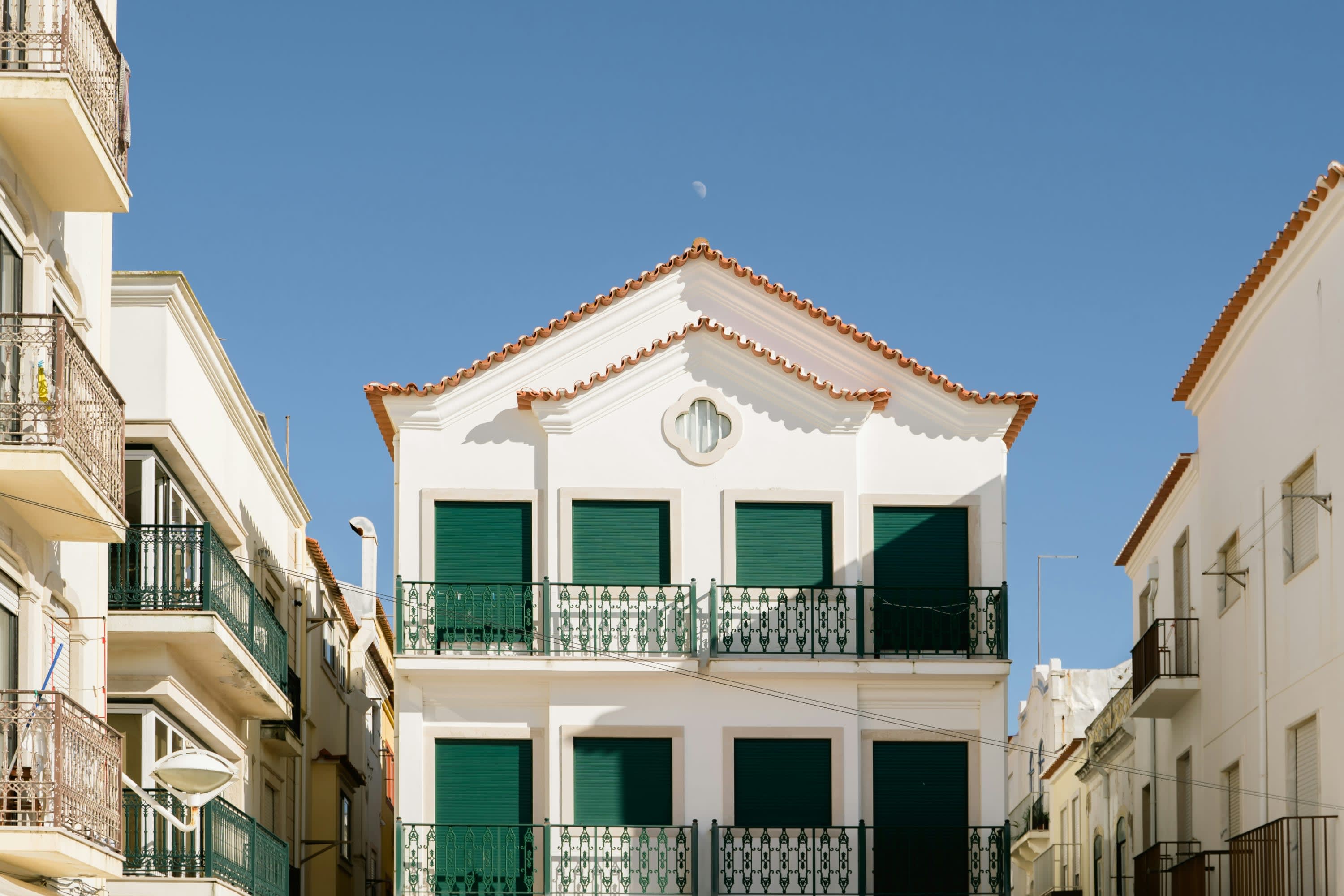 A historic building with orange Portuguese roof tiles, green shutters and a black wrought-iron railing along its balconies