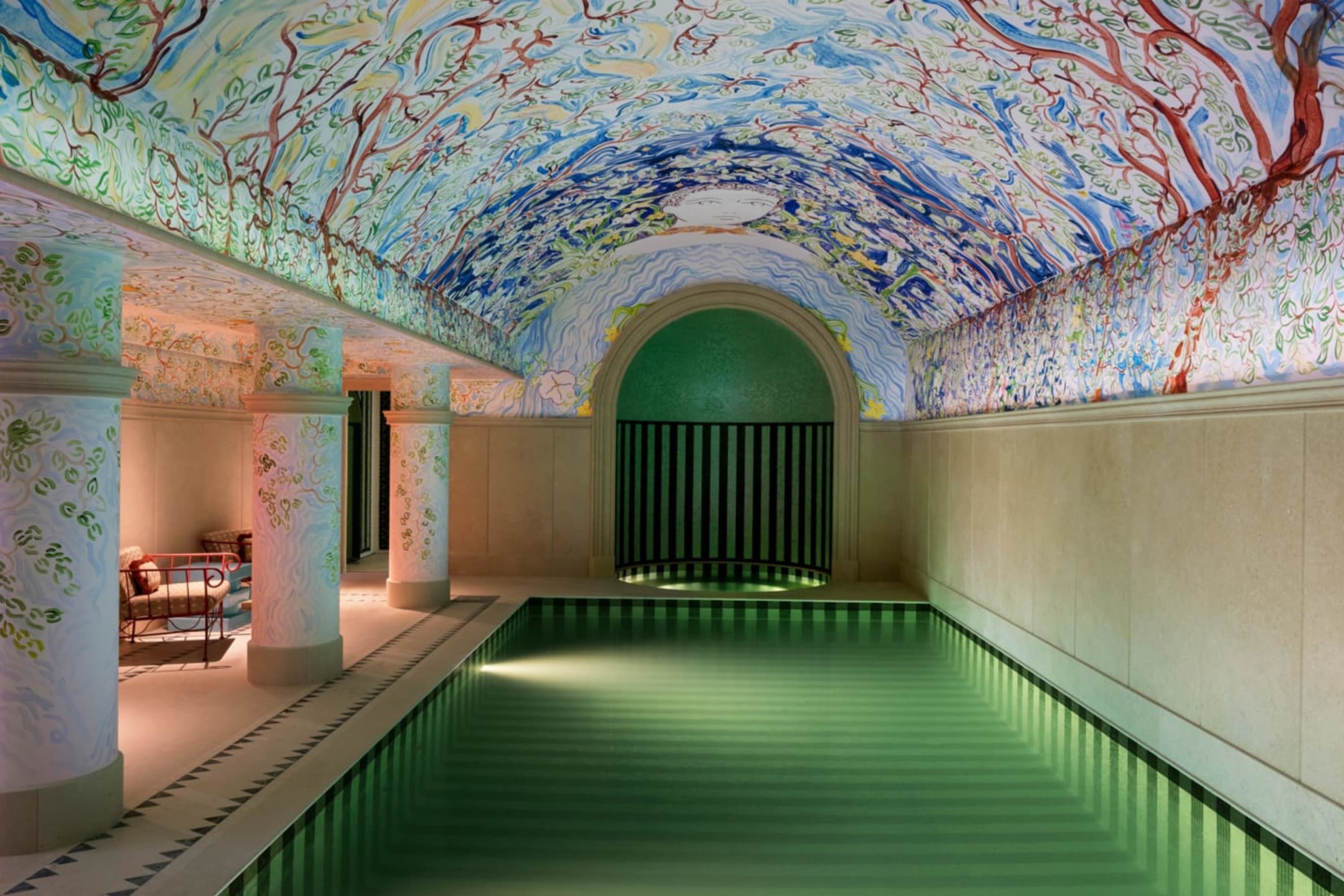 Roman bathhouse-style indoor pool with a vibrant, almost rainbow mural on a semi-domed tile ceiling, thick columns and a saltwater pool
