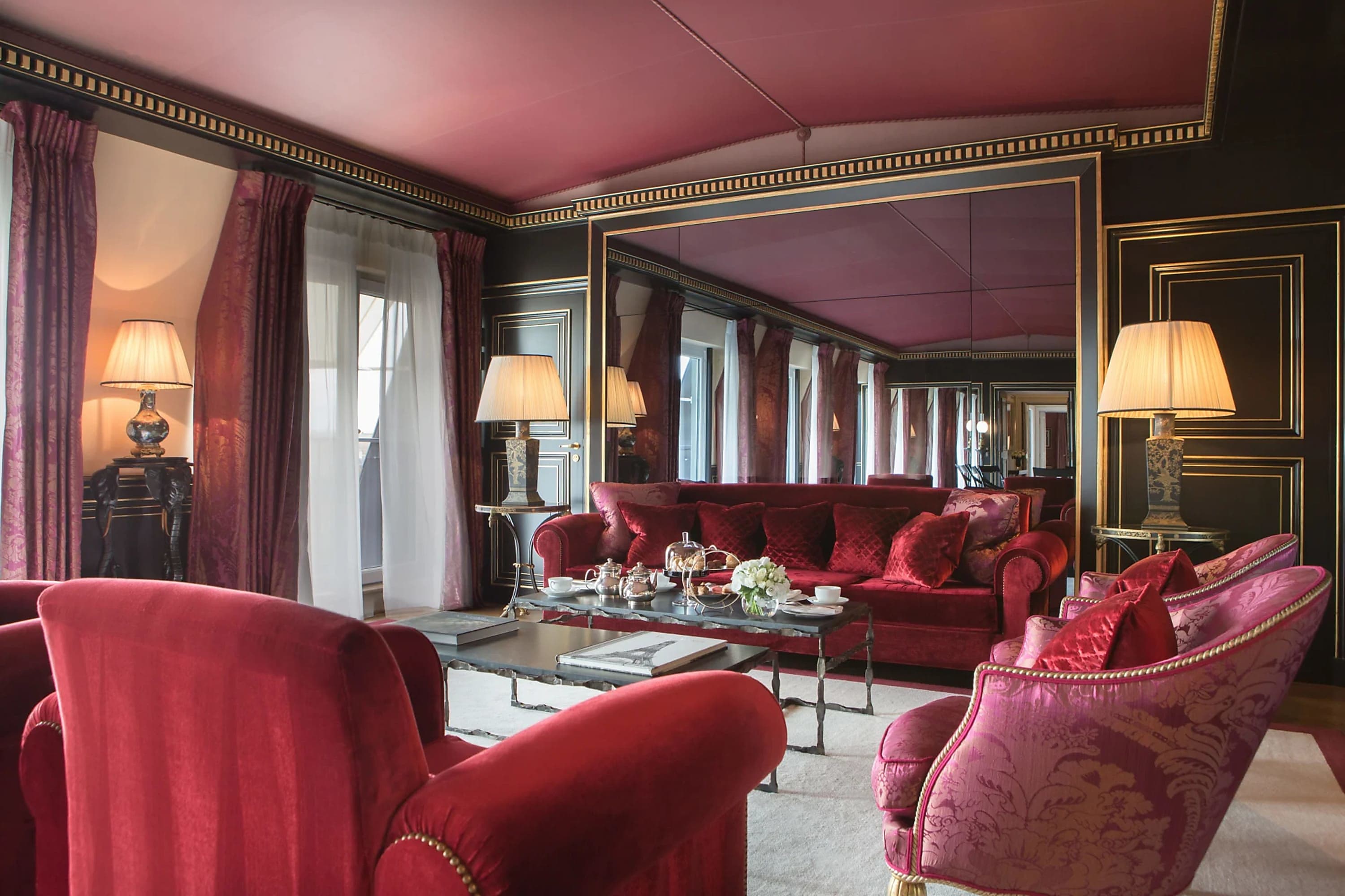 Art Deco-themed and slightly moody living room with lots of red or burgundy fabrics contrasting with a white carpet and gold lamps