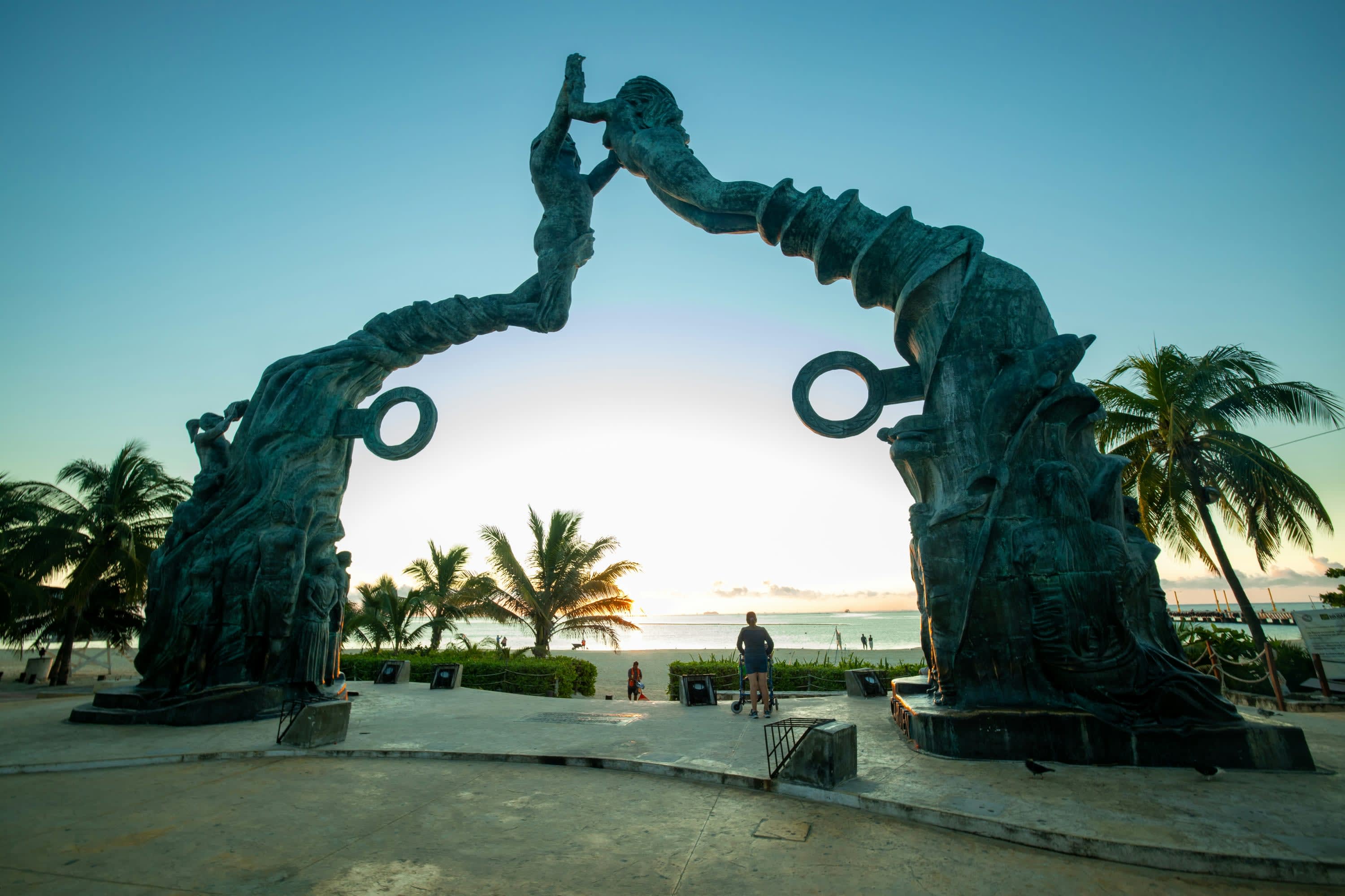 Abstract statue of mermaids forming an arch on a beach with palm trees