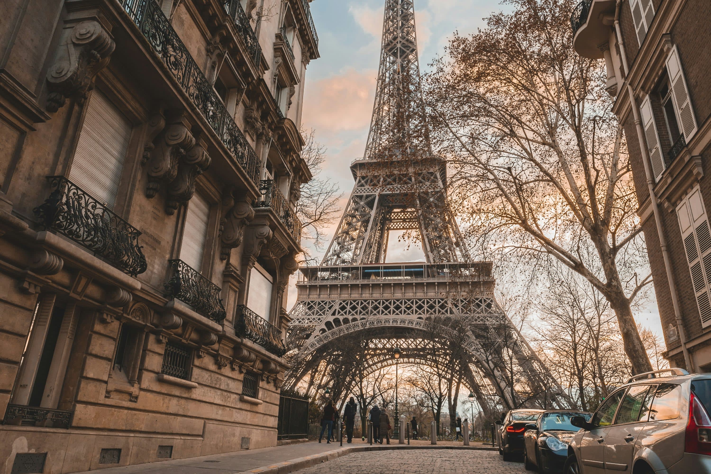 A ground view of the Eiffel Tower, focusing on its lower structure and framed by historic buildings