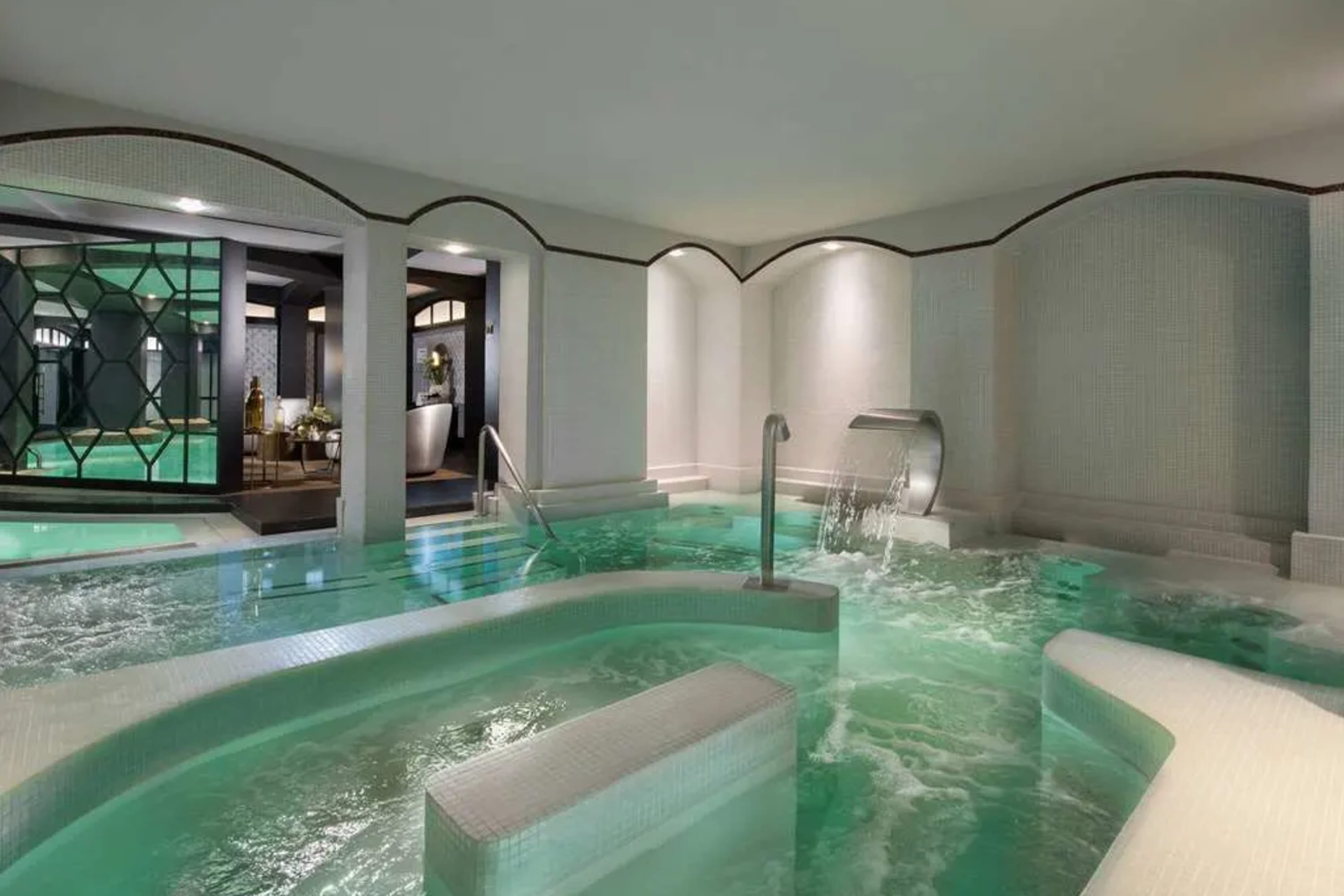 A pool-size hot tub with jets disturbing the water in an elegant bathhouse-like pool area