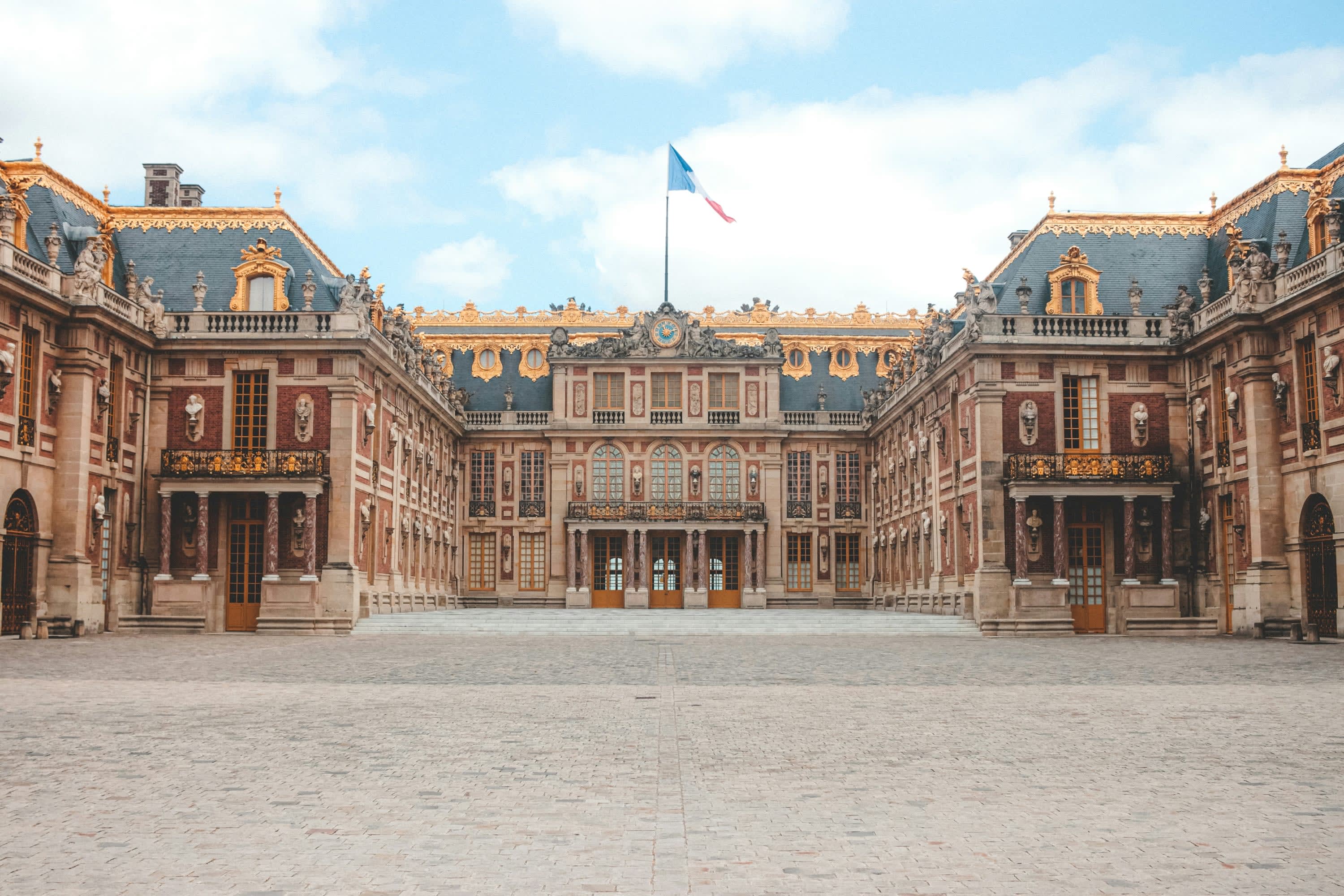 Grandiose architecture of the Palace of Versailles across a large stone plaza