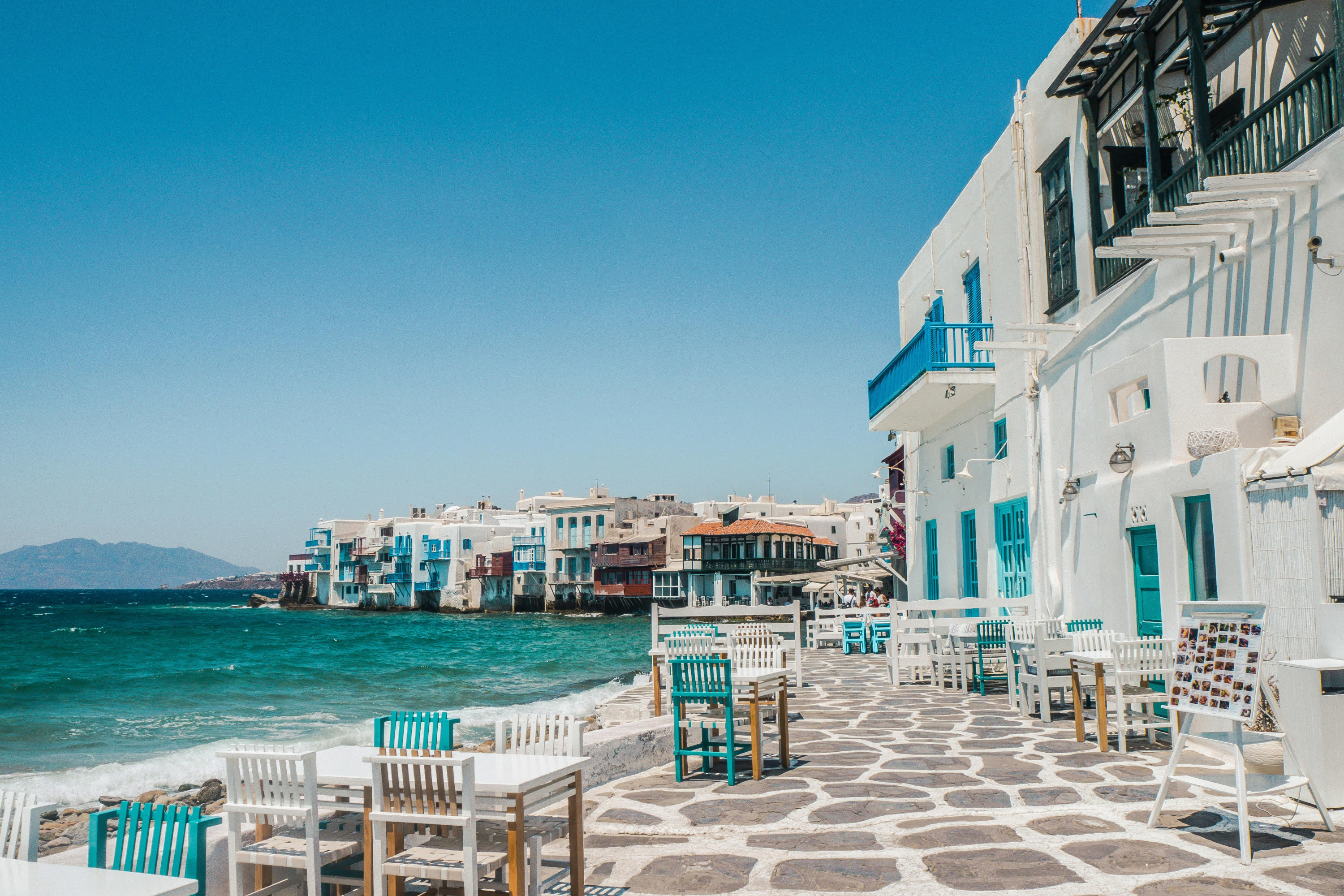 A waterfront promenade area with whitewashed buildings with turquoise accents that match the water