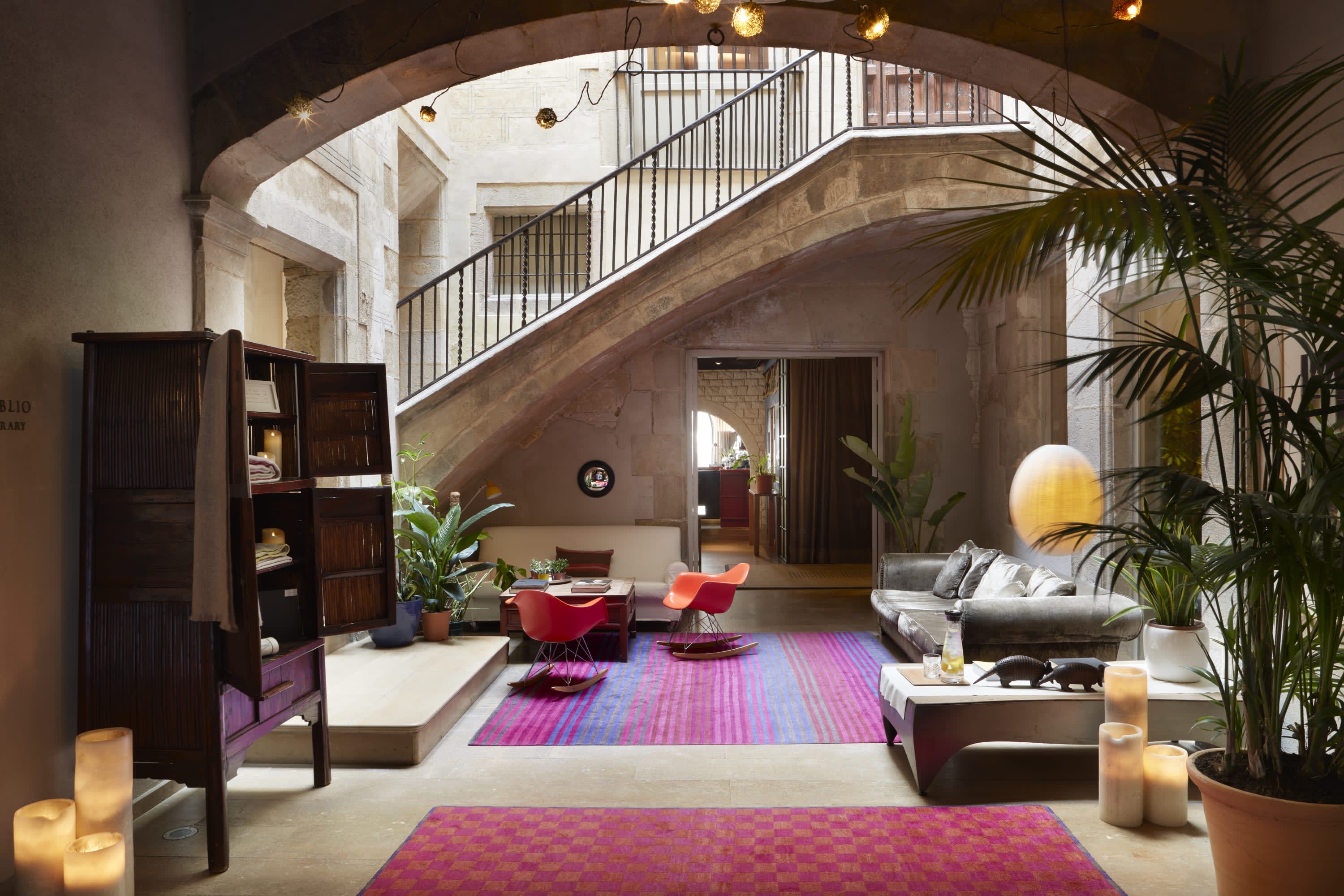 Bright contemporary fabrics and posh furnishings contrast with a historic stone-and-iron staircase and stone walls in a large lounge-like space