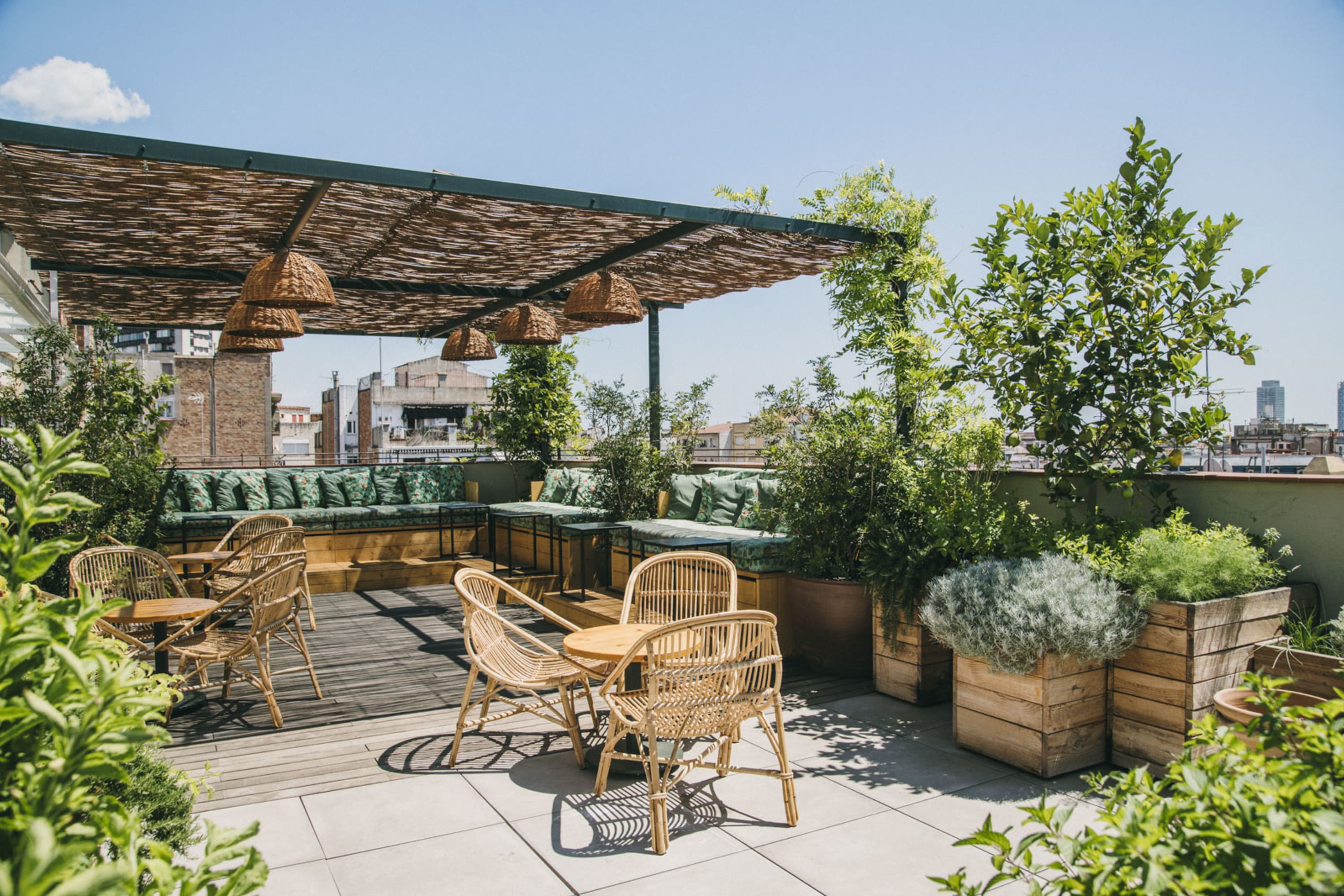 Chic rooftop terrace space with lots of potted plants, a contemporary awning with wicker or thatch slats and wooden chairs and tables