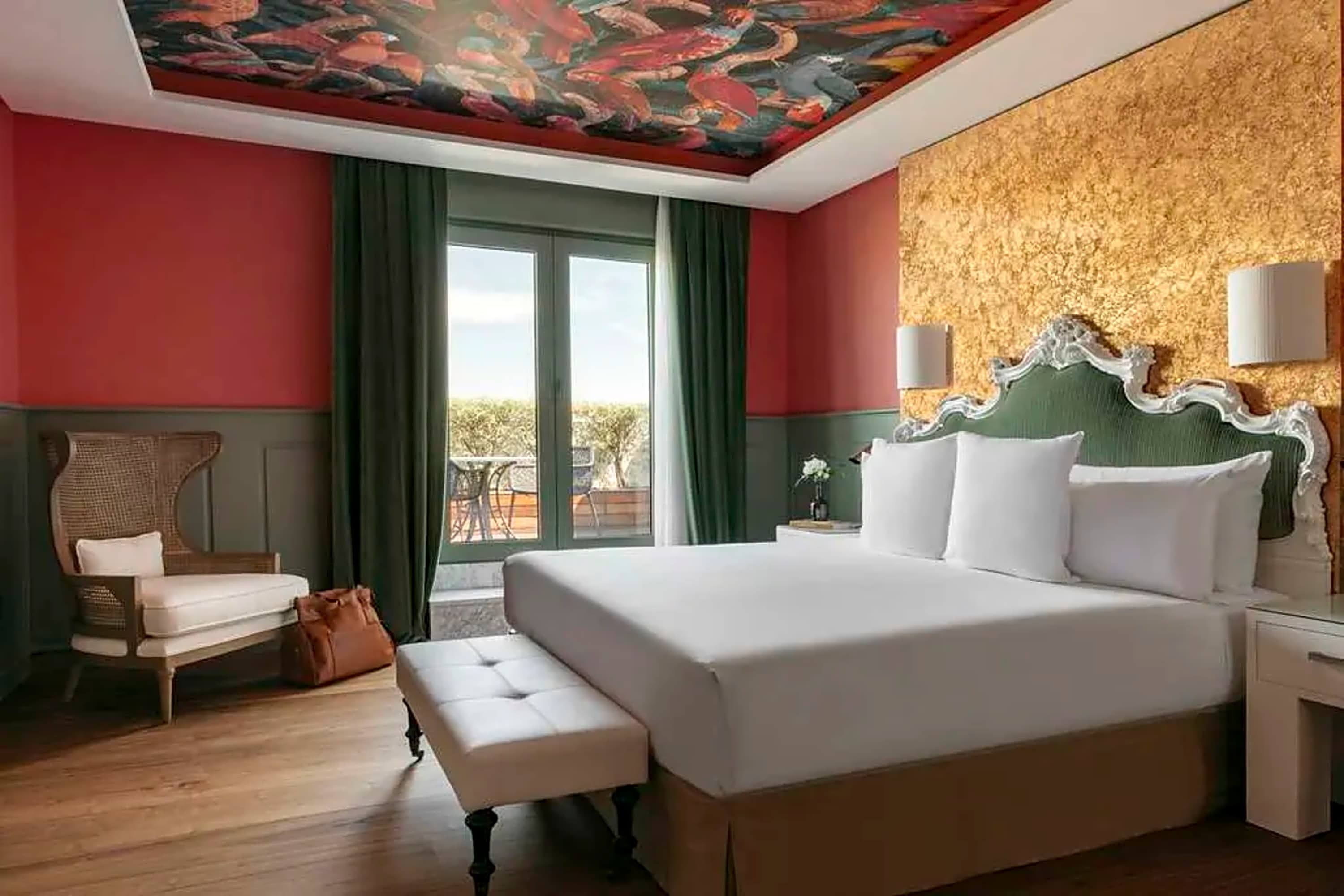Artful hotel room with a mural on the ceiling, a chic balcony setup and a heavy use of red, green and golds