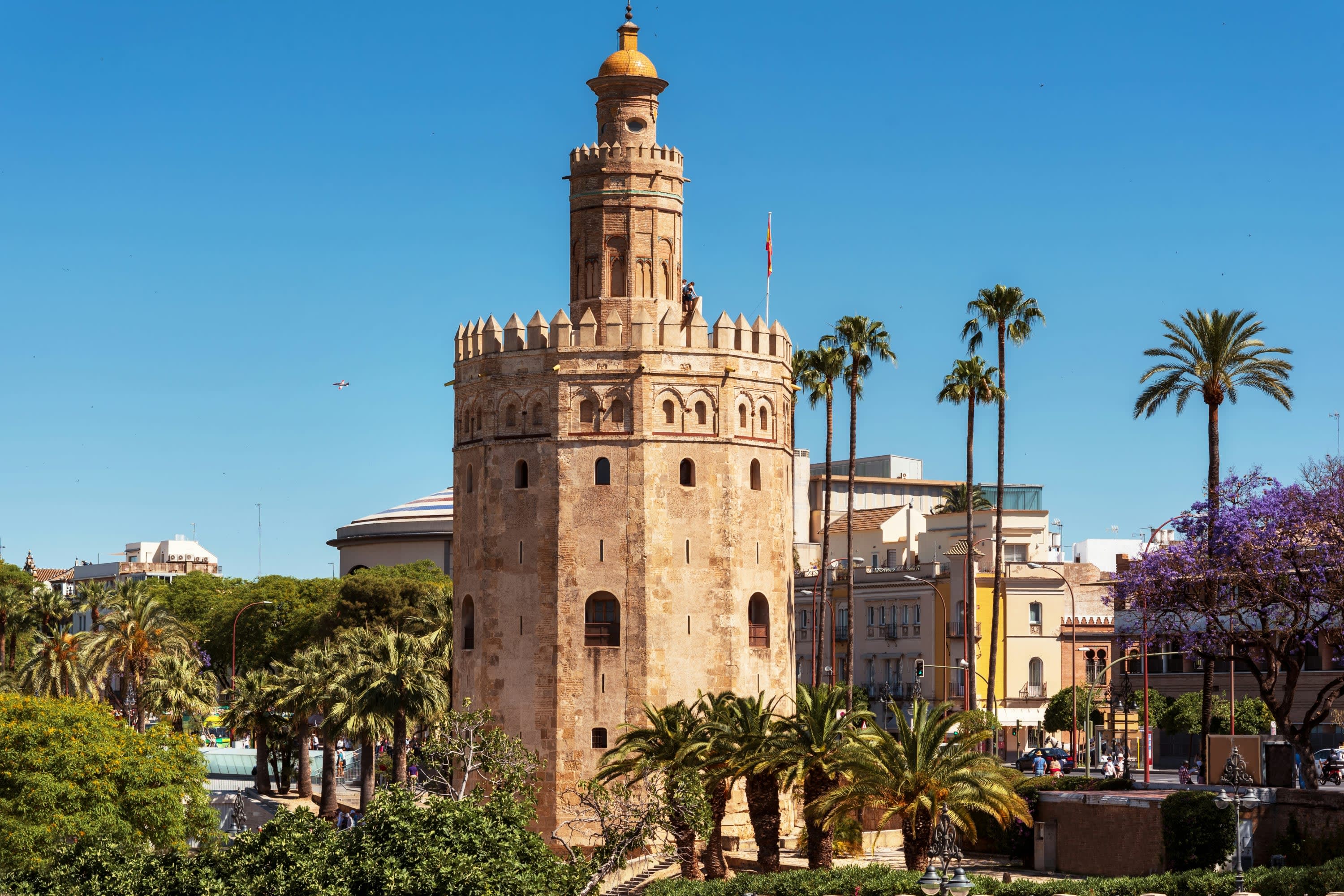A massive stone watchtower surrounded by palm trees on a sunny day in Seville